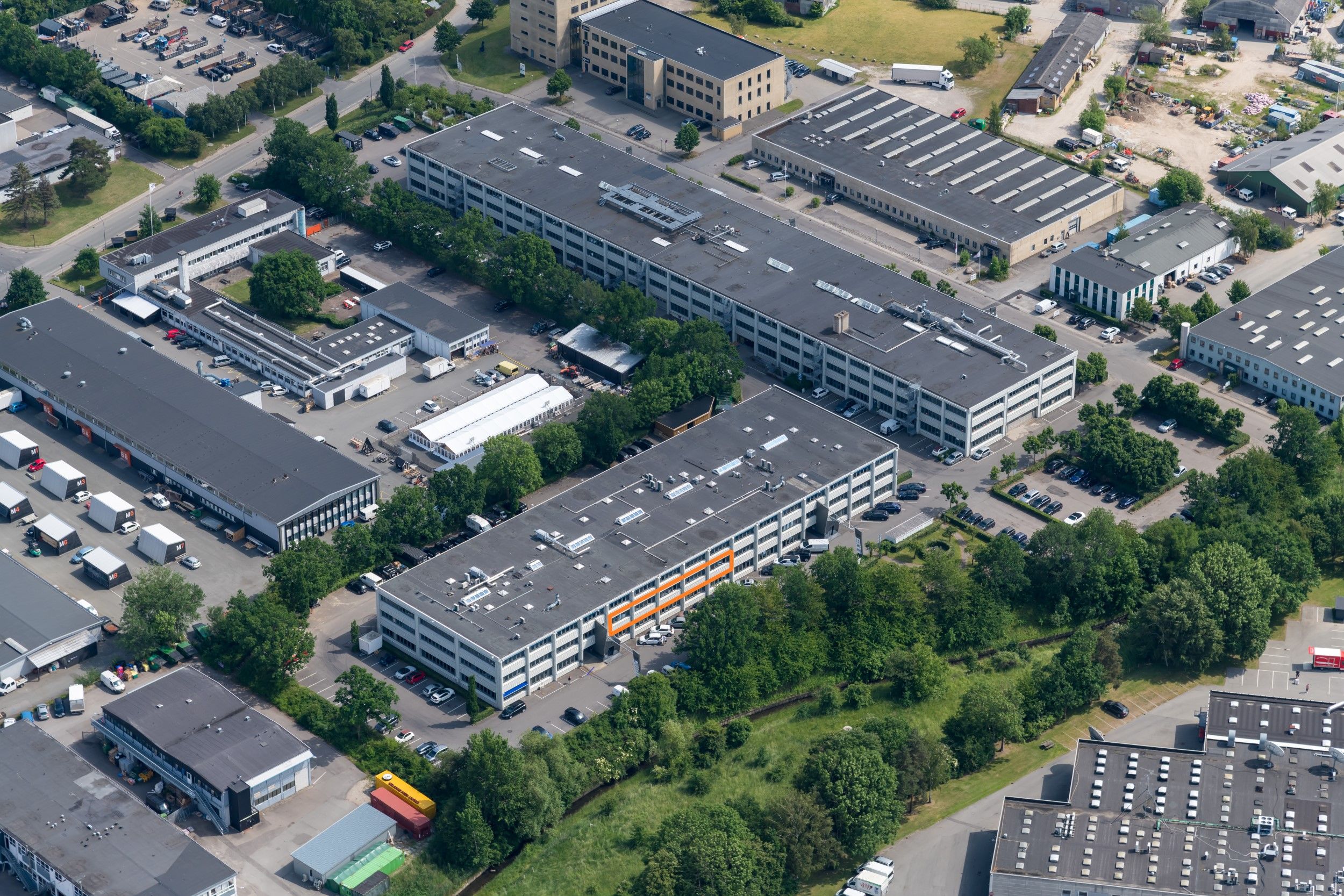 Fabrikbygninger med parkeringspladser og busser samt store containere med M-logo på dem