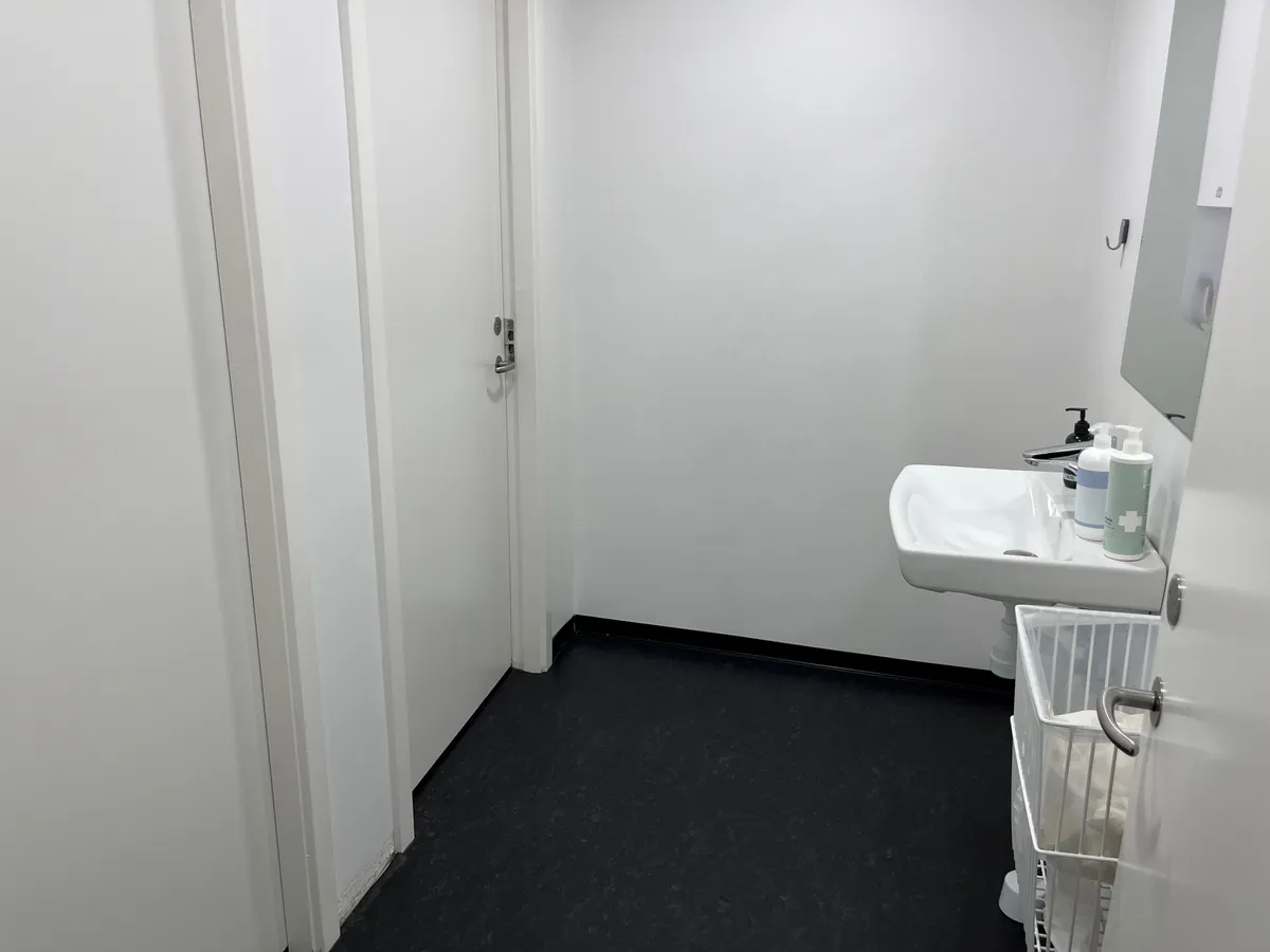 Ledig toiletrum med hvidt klædt væg og sort gulv samt hvidt toilet og spejl med to rengøringsmidler