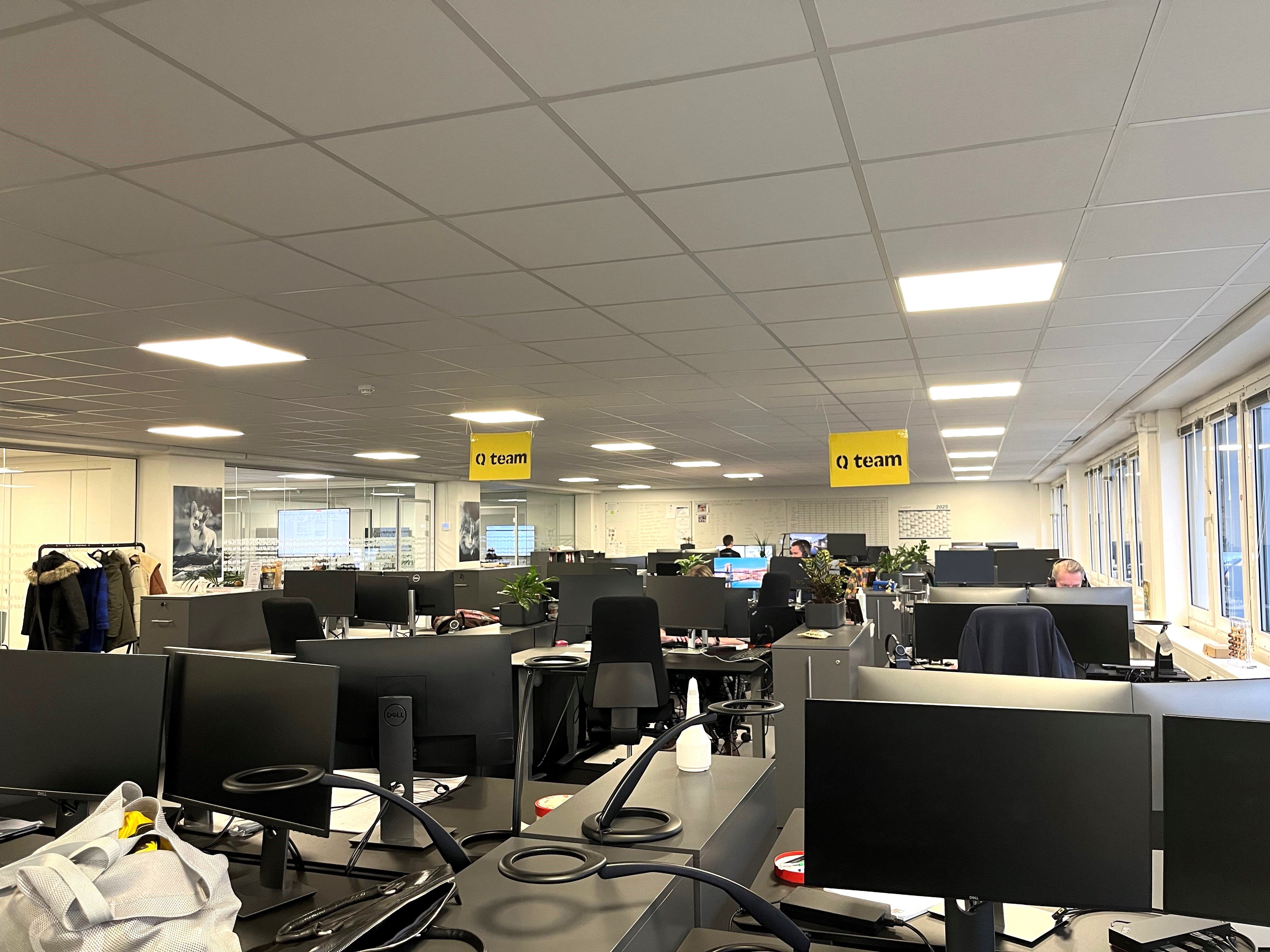 Kontorlokaler med computere, stole, planter, og en sætte med tøj hængende på en klædhænger nederste højre hjørne