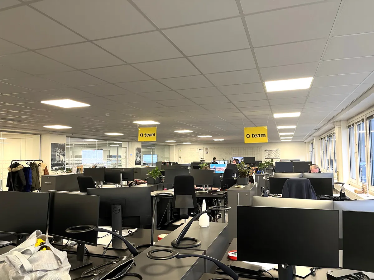 Kontorlokaler med computere, stole, planter, og en sætte med tøj hængende på en klædhænger nederste højre hjørne