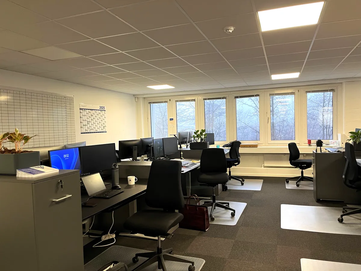 Kontor med fire skriveborde med hver sin computer, fire stolpe og fire kaffekopper, samt fire plantepoter