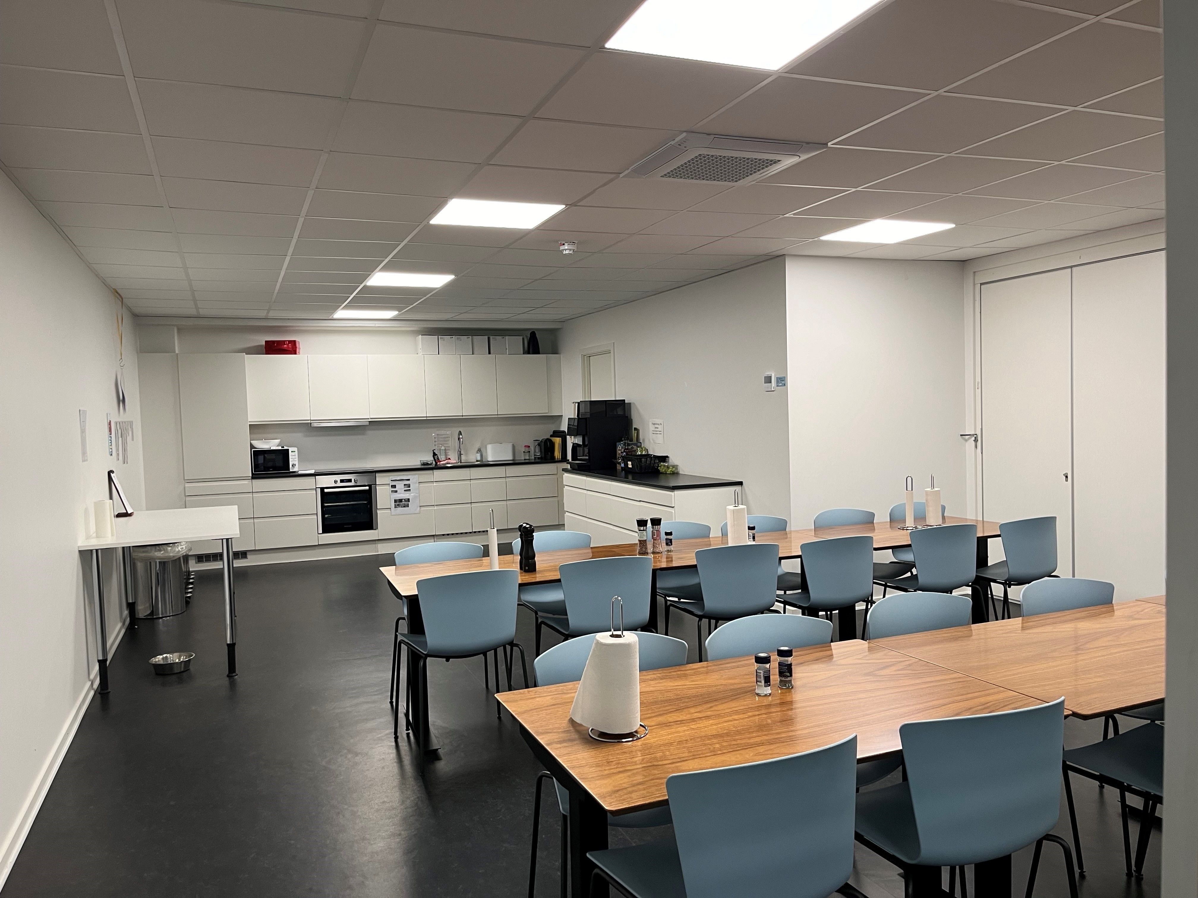 Moderne kontor med hvide vægge, lyse lofter, lyse og træborde med blå stole og nye klimaanlæg og køkkenudstyr