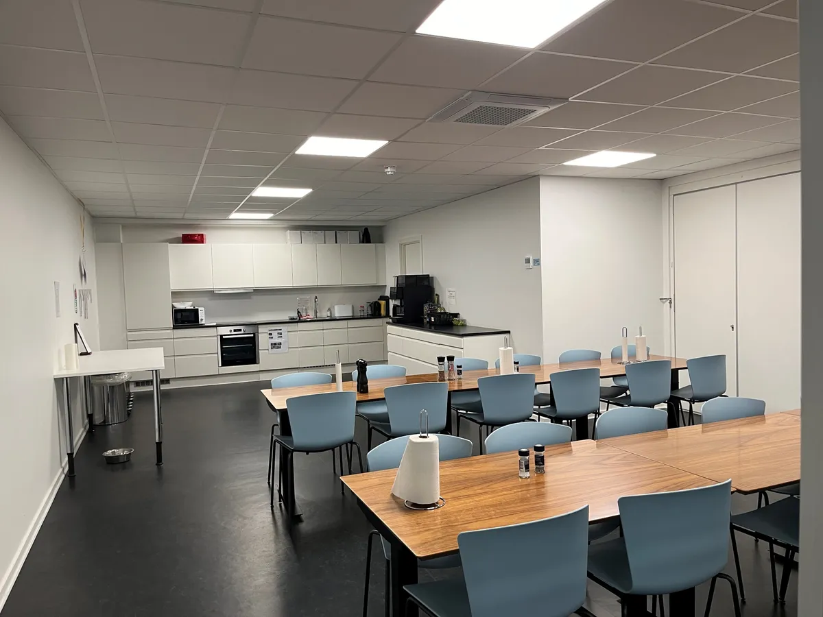 Moderne kontor med hvide vægge, lyse lofter, lyse og træborde med blå stole og nye klimaanlæg og køkkenudstyr