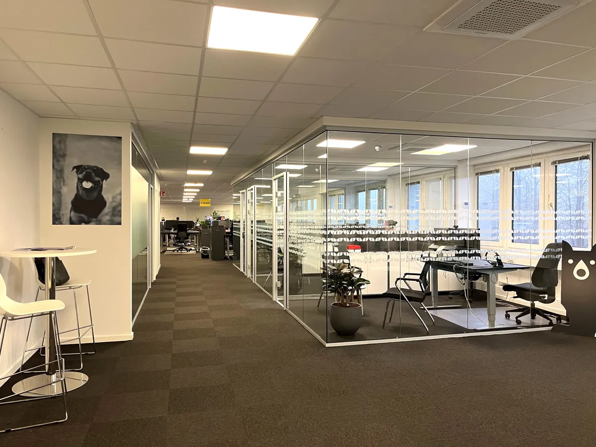 Kontorrum med møbler og skriveborde, hvilende i et moderne kontor med glasvægge og tavle med hundebillede. Luftcondition og