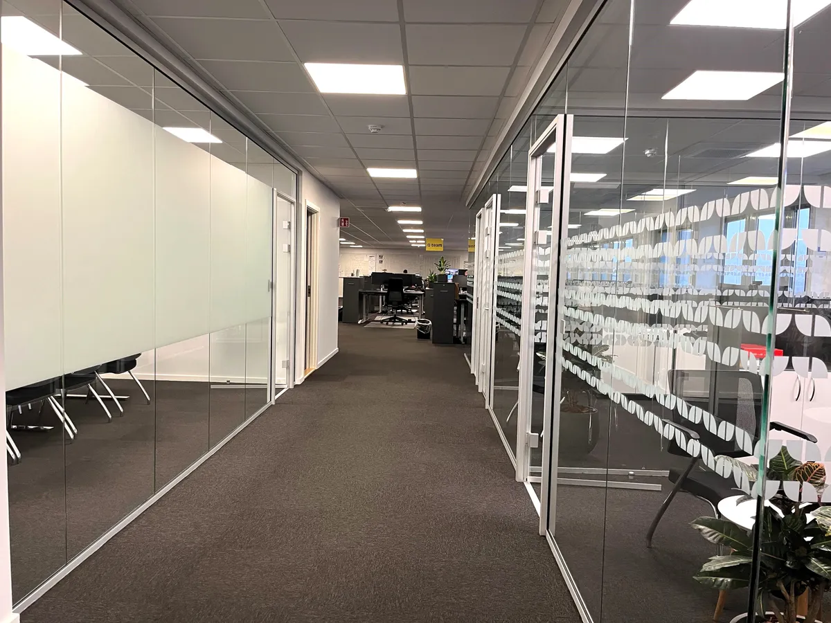 Moderne kontor med glasvægge og højt loft, hvor højttalere og kameraer er installeret til sikkerhed. En lille gruppe