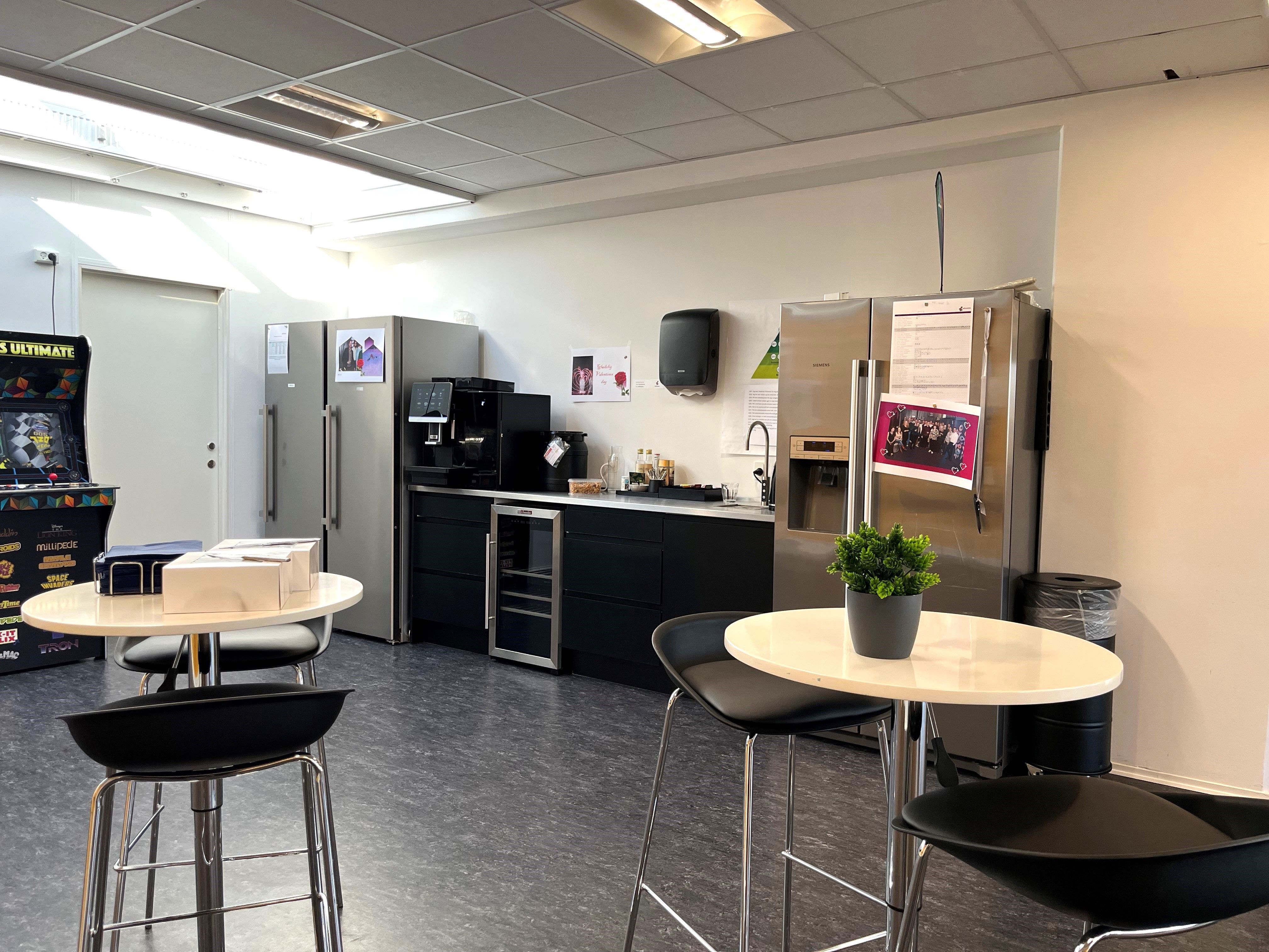 Kontor med flere stole, to runde borde med pebermynteplanter og to køleskabe med kaffemaskine, ovn og håndvask
