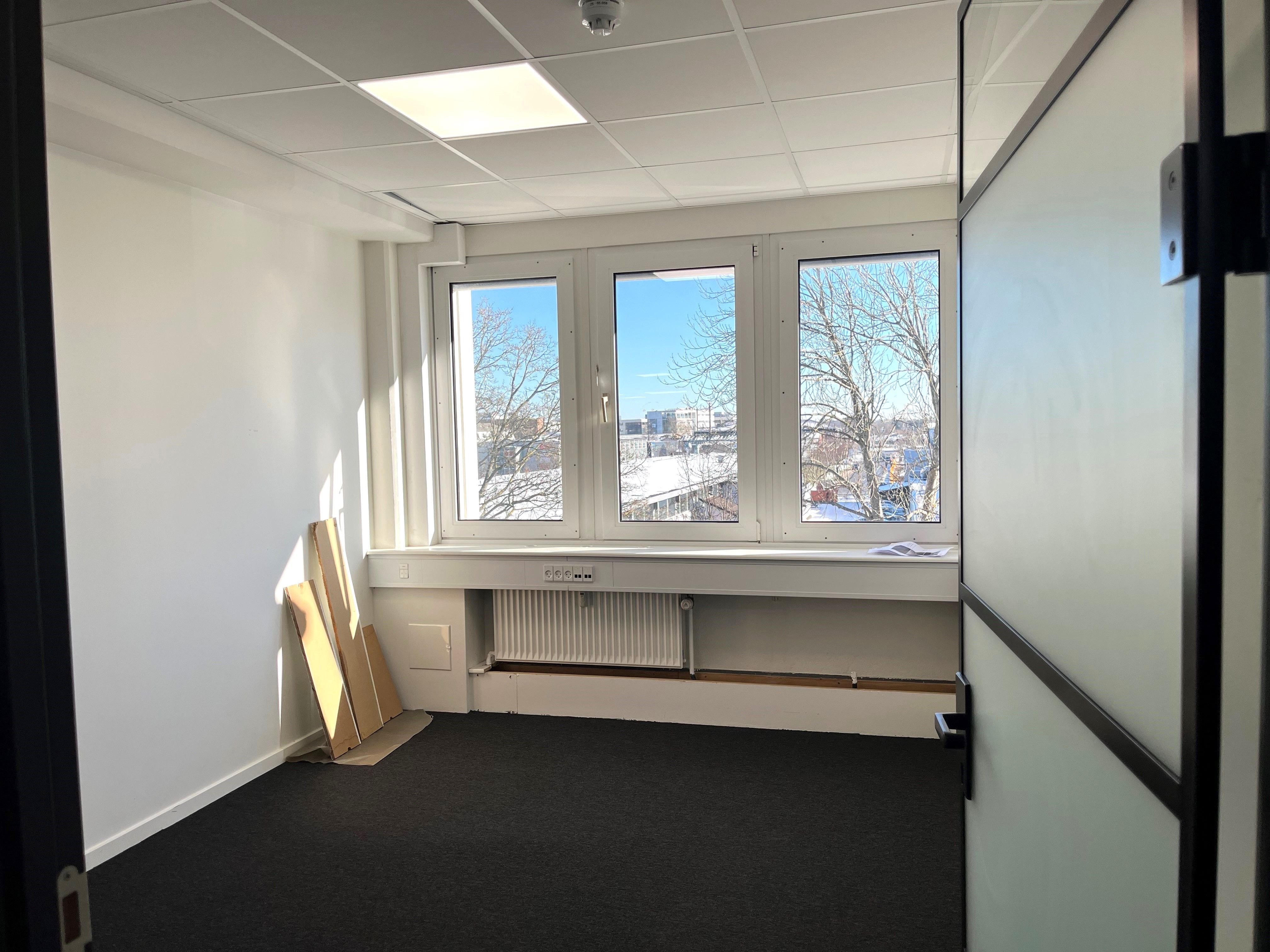 Kontor med højt hvælvet loft, lyse vinduer og naturligt lys. Værelse med smukke glasløsninger og radiator under vinduet.