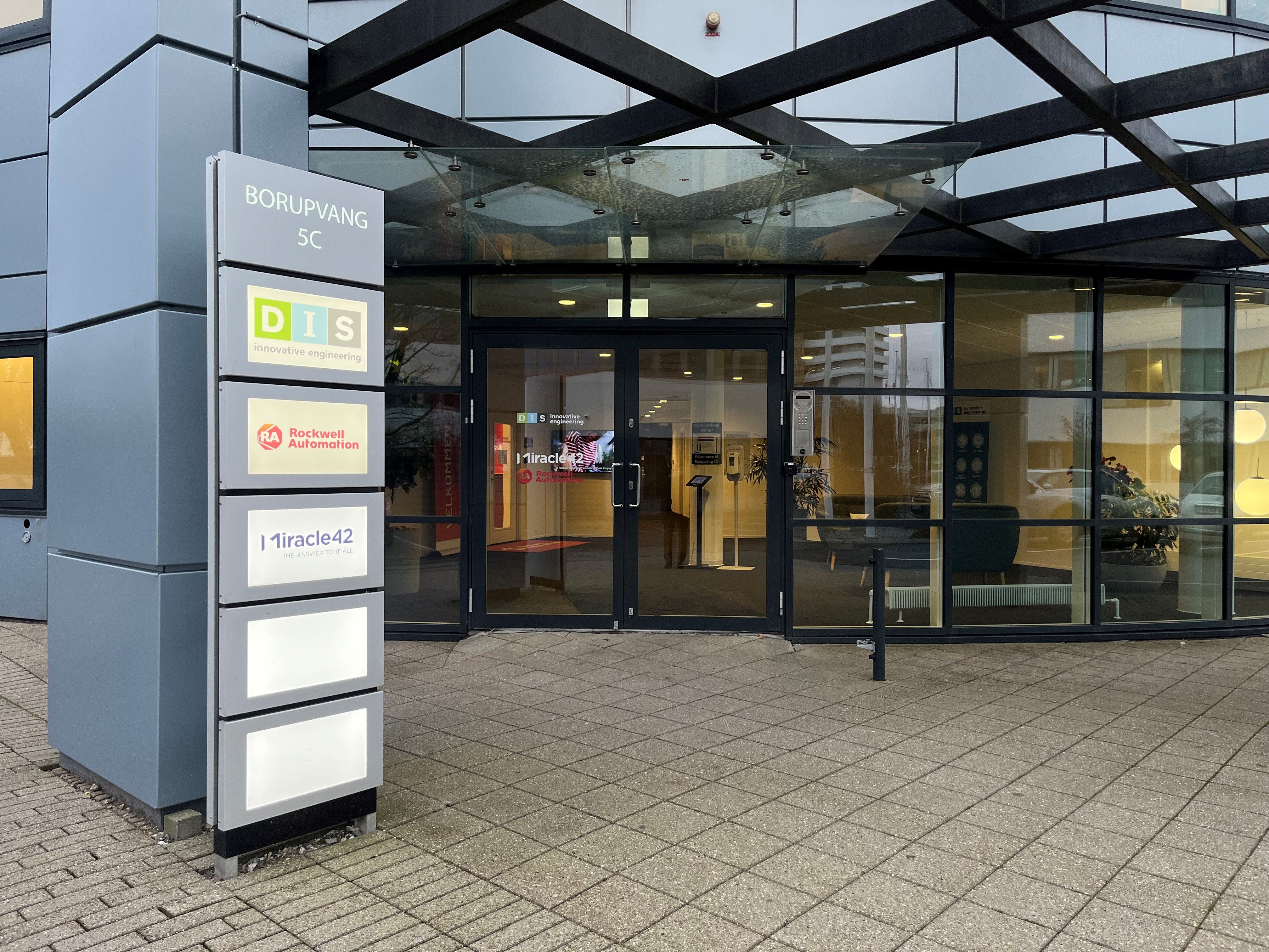 Forside med navneskilte på gulv, foran en stor, glas- og stålbygning, med teksten Borupvang 5C, DIS og Rockwell Automation