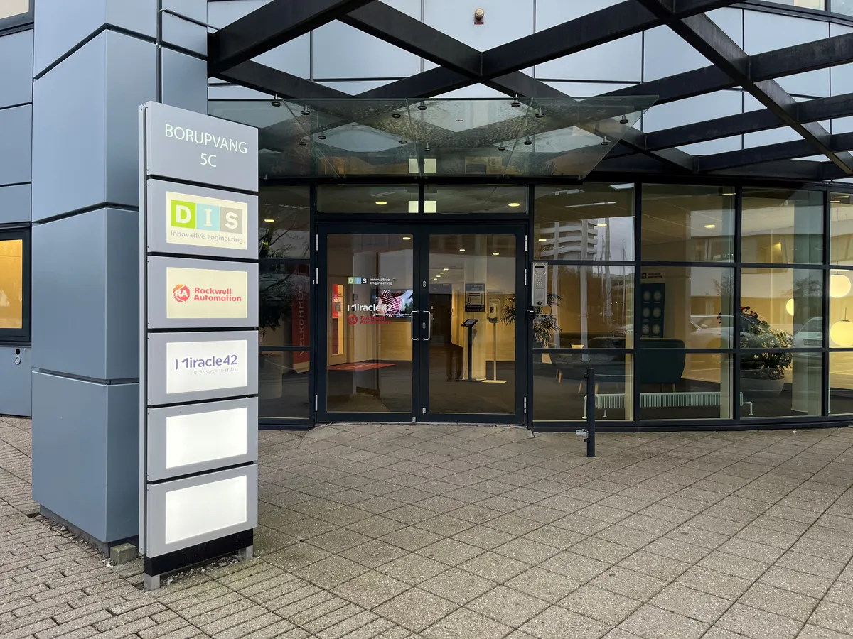 Forside med navneskilte på gulv, foran en stor, glas- og stålbygning, med teksten Borupvang 5C, DIS og Rockwell Automation