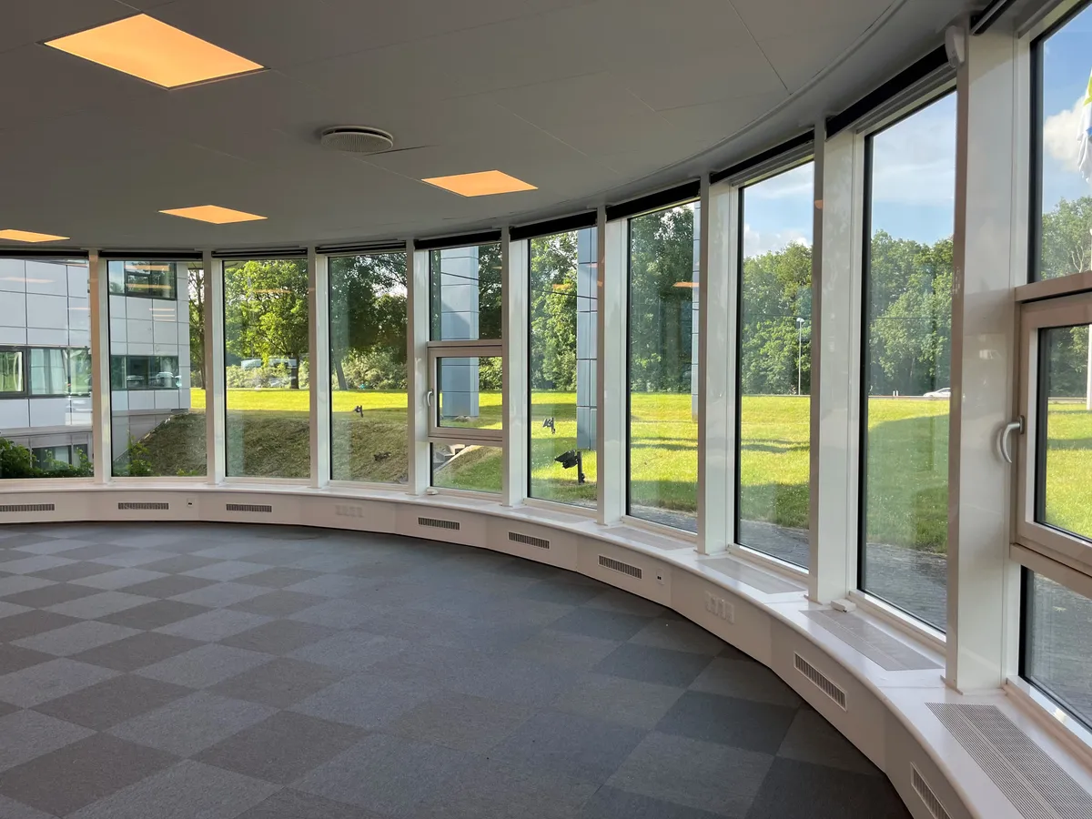 Kontor med store vinduer, runde gulv mønstre, hvide vægge, grønne områder udenfor og flere bygninger i baggrunden