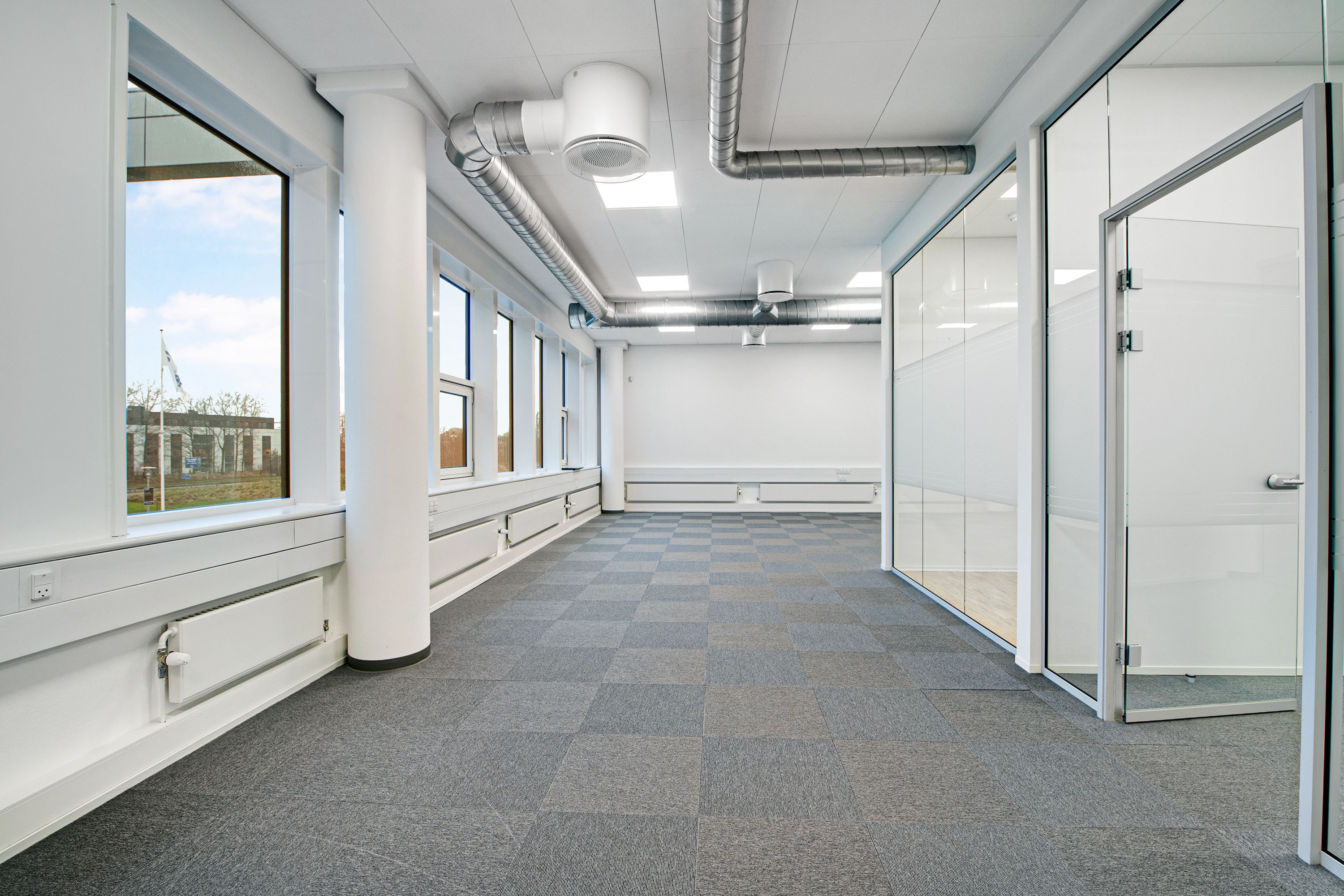 Kontor med hvide vægge, glasvinduer, tæppegulv og stålrør. Højt til loftet, med lysepunkter og tæppegulv. Glasdøre med