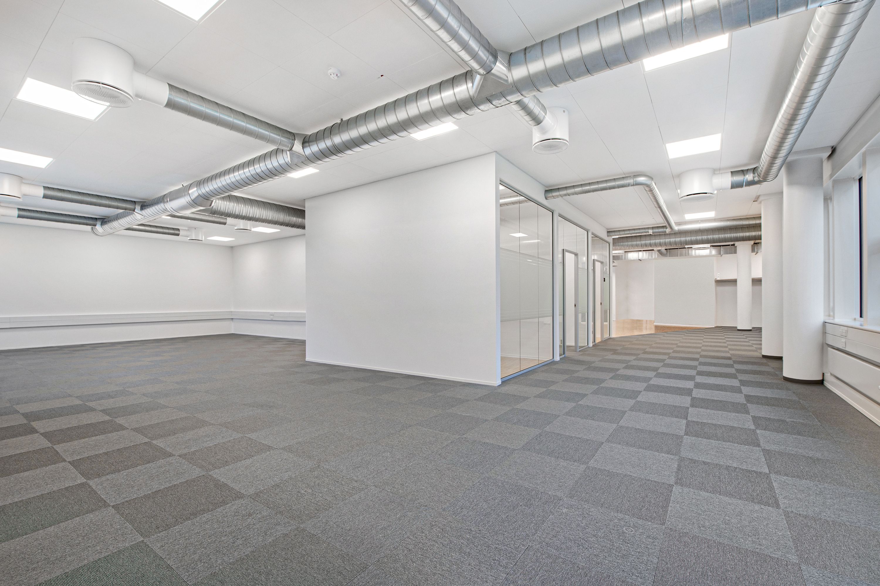 Hvidt, rummeligt kontor med glasvægge og krydsformede gulvfliser, moderne loft med indlejrede lysekroner og ventiler