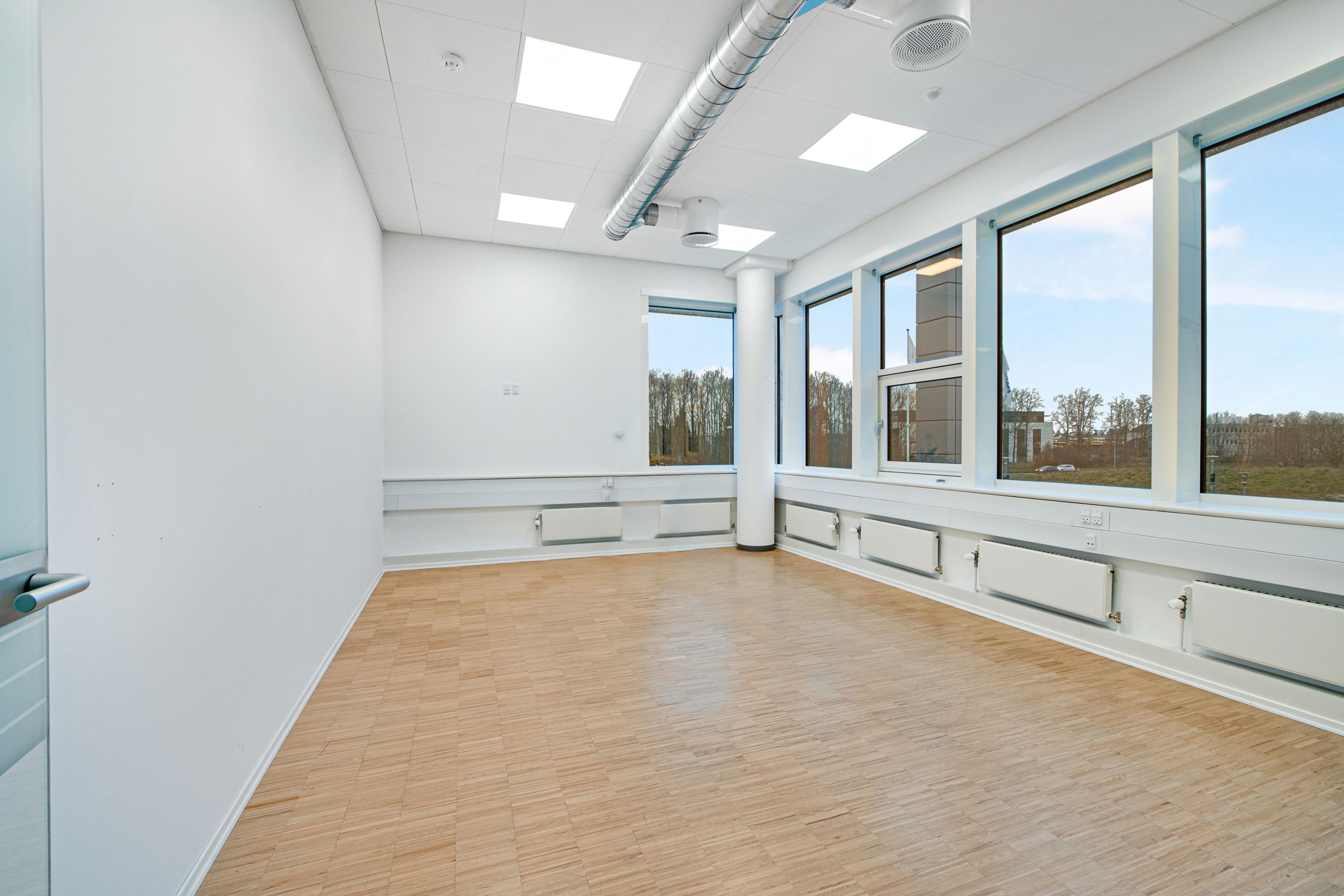 Kontor med hvide vægge, gulv og loft, vinduer med glas og hvide indramninger, radiatorer og ventiler på væggen,