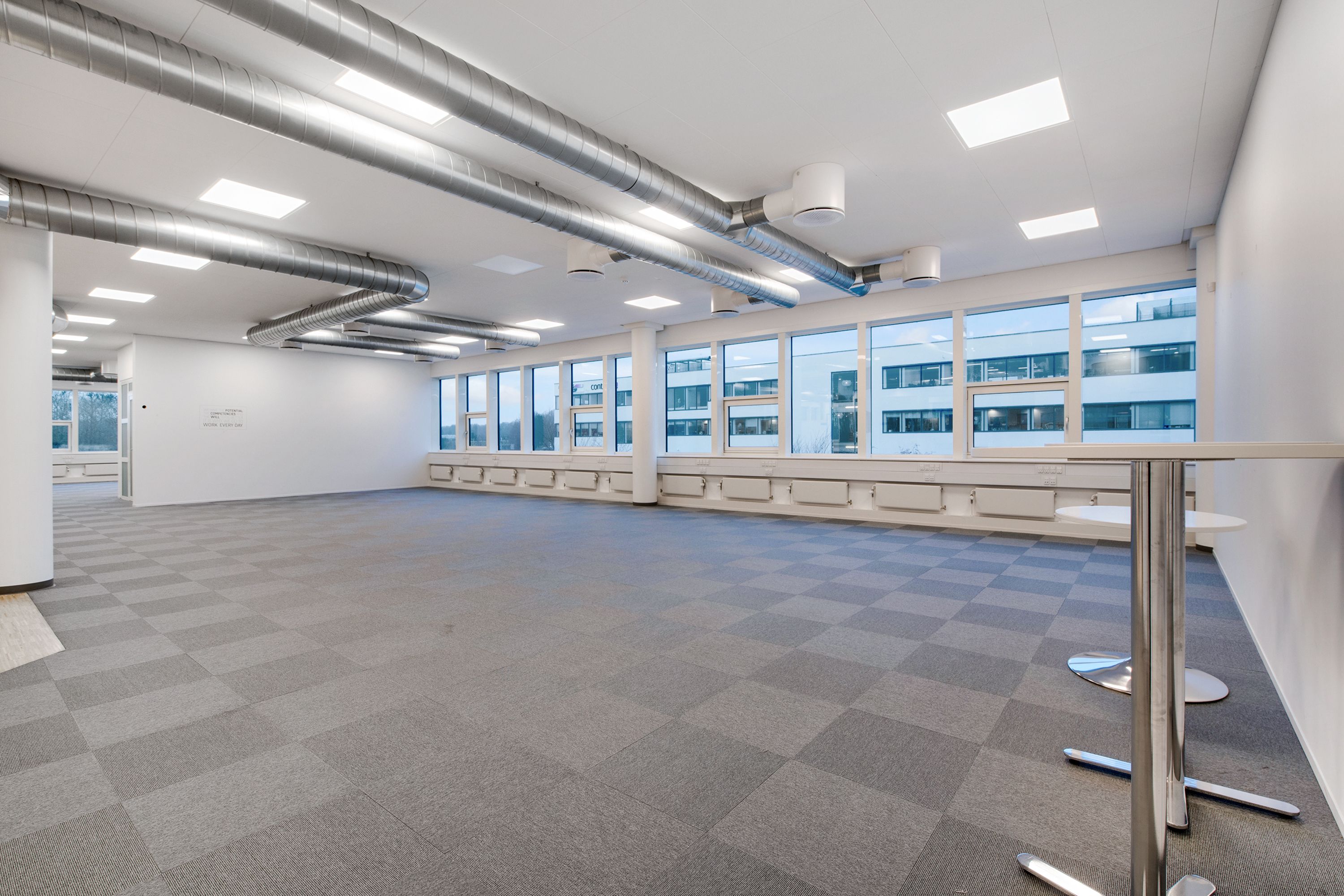 Et moderne kontorrum med møbler og møntfrie gulv. Væggene er hvide, og der er mange vinduer. Loftet er hvidt med store runde