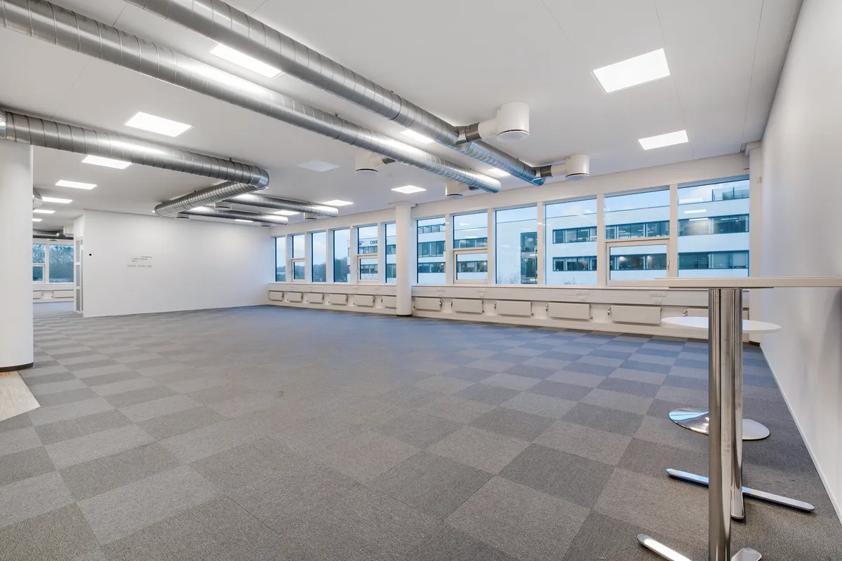 Et moderne kontorrum med møbler og møntfrie gulv. Væggene er hvide, og der er mange vinduer. Loftet er hvidt med store runde