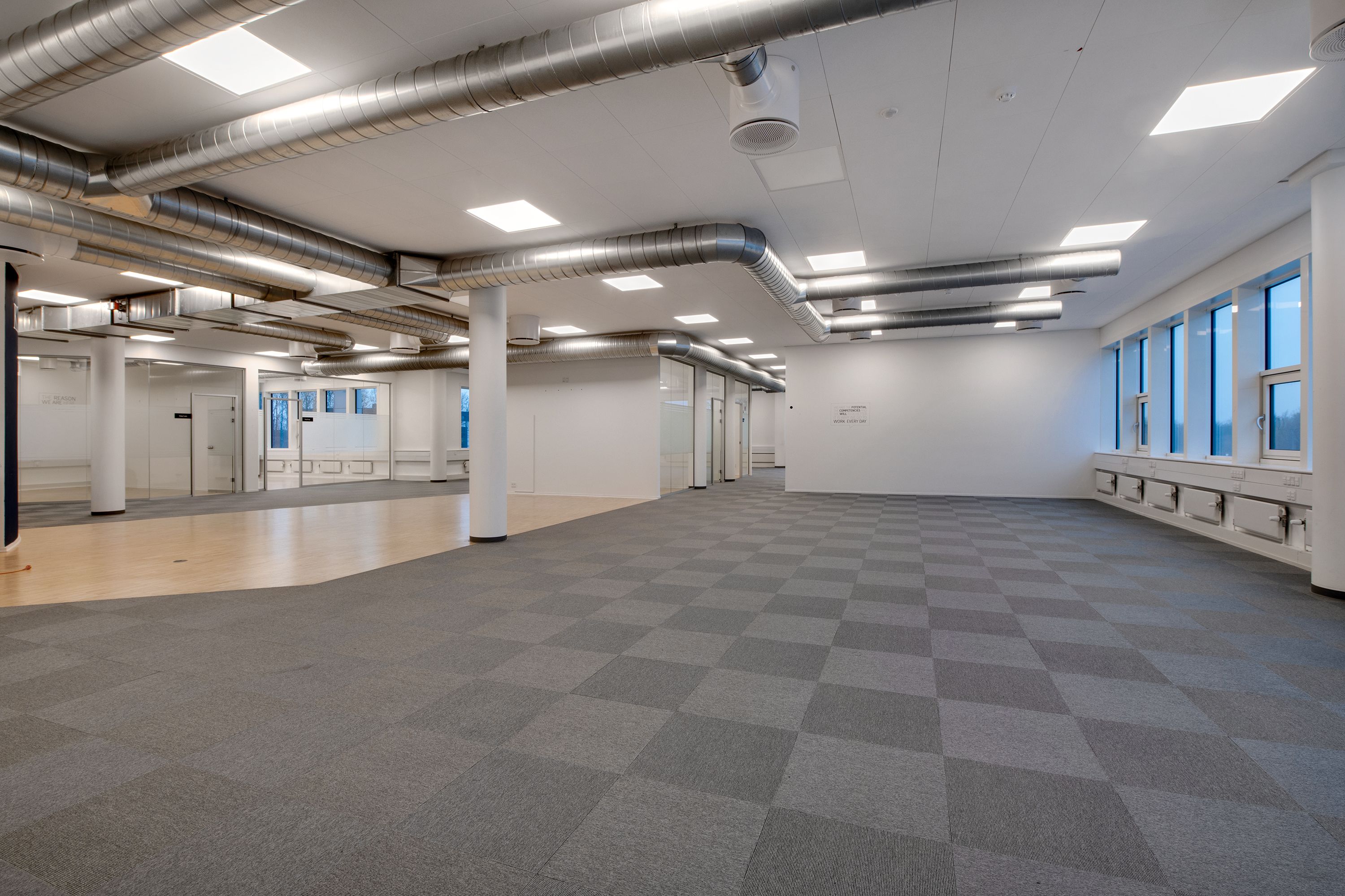 Et moderne kontor med krydsfinergulve, hvide vægge, møbler og store vinduer med glaspergolaer