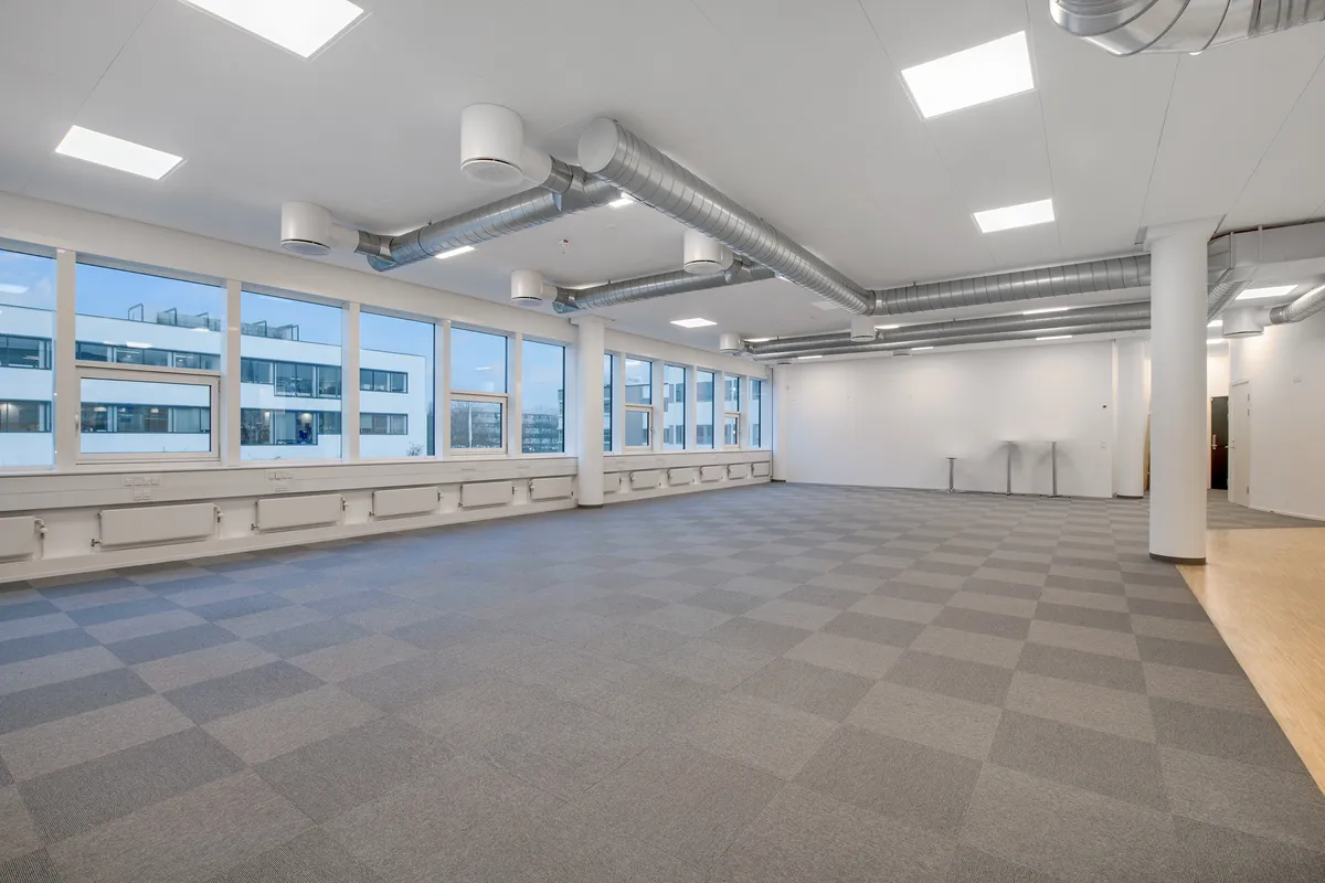 Røgsugtt med ventiler og gulvbelægning i en kontorfællesskab med vinduer mod bygningen udenfor og lyse loftslamper