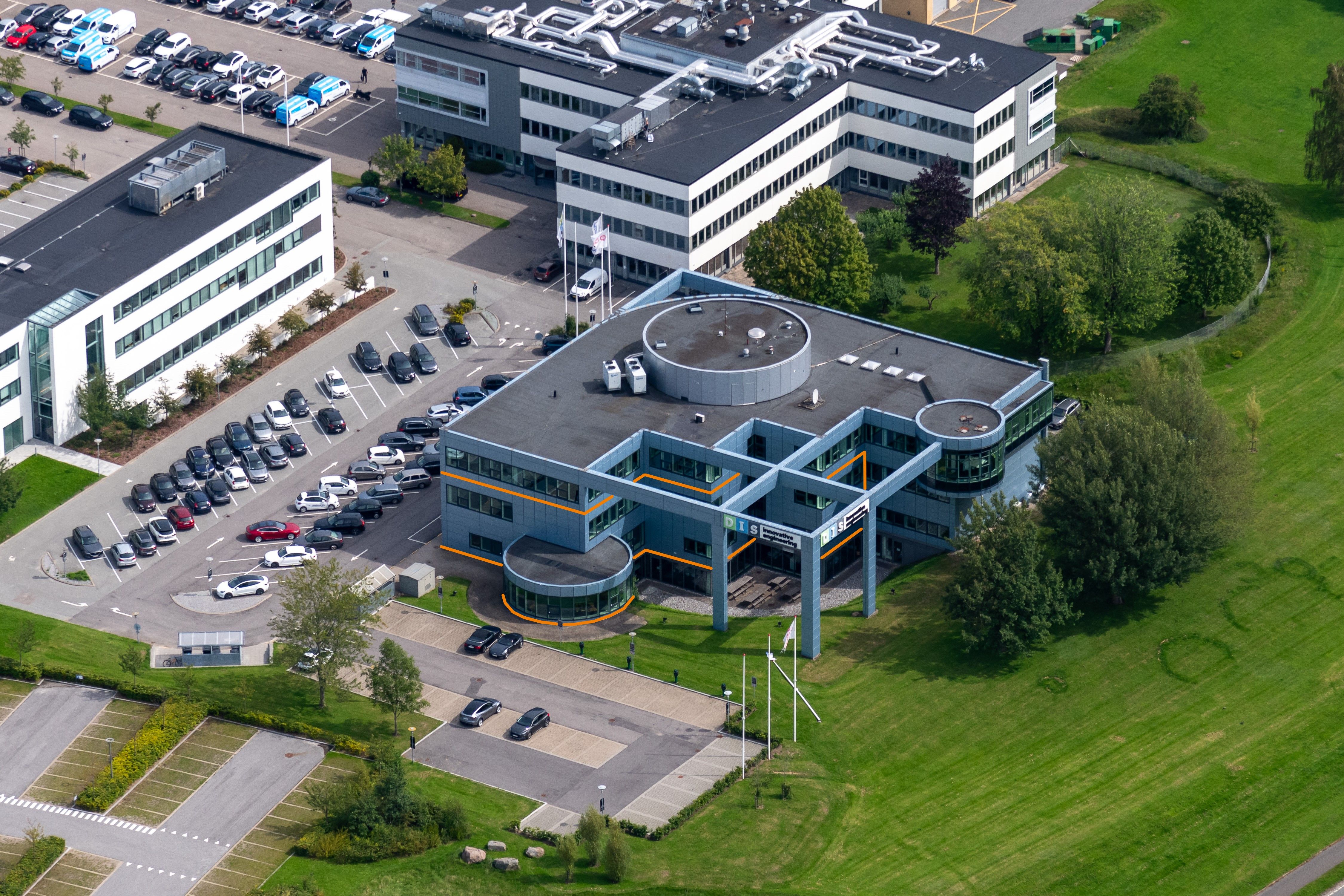 En luftfotovisning af et stort firma med mange parkerede biler og et kæmpe parkeringsområde