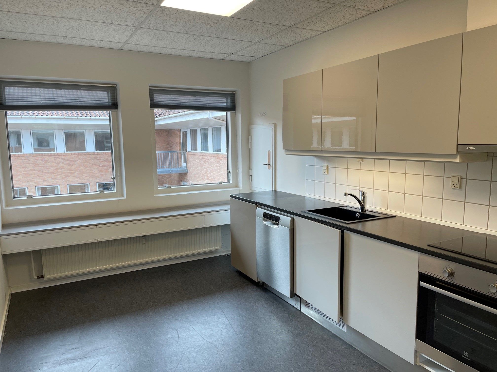 Pænt og velholdt kontor med moderne køkken og to store vinduer med udsigt over bygning og gadegejle i Hillerød. Moderne