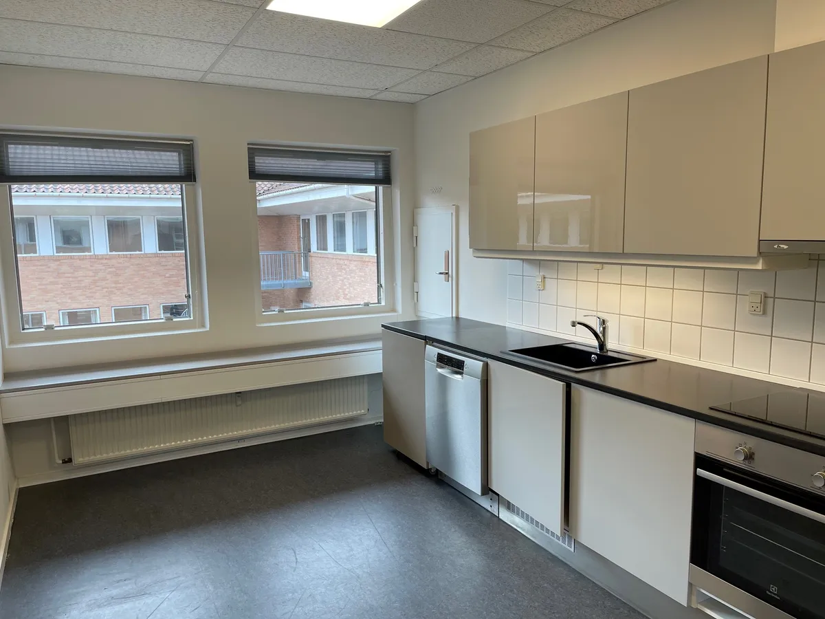 Pænt og velholdt kontor med moderne køkken og to store vinduer med udsigt over bygning og gadegejle i Hillerød. Moderne