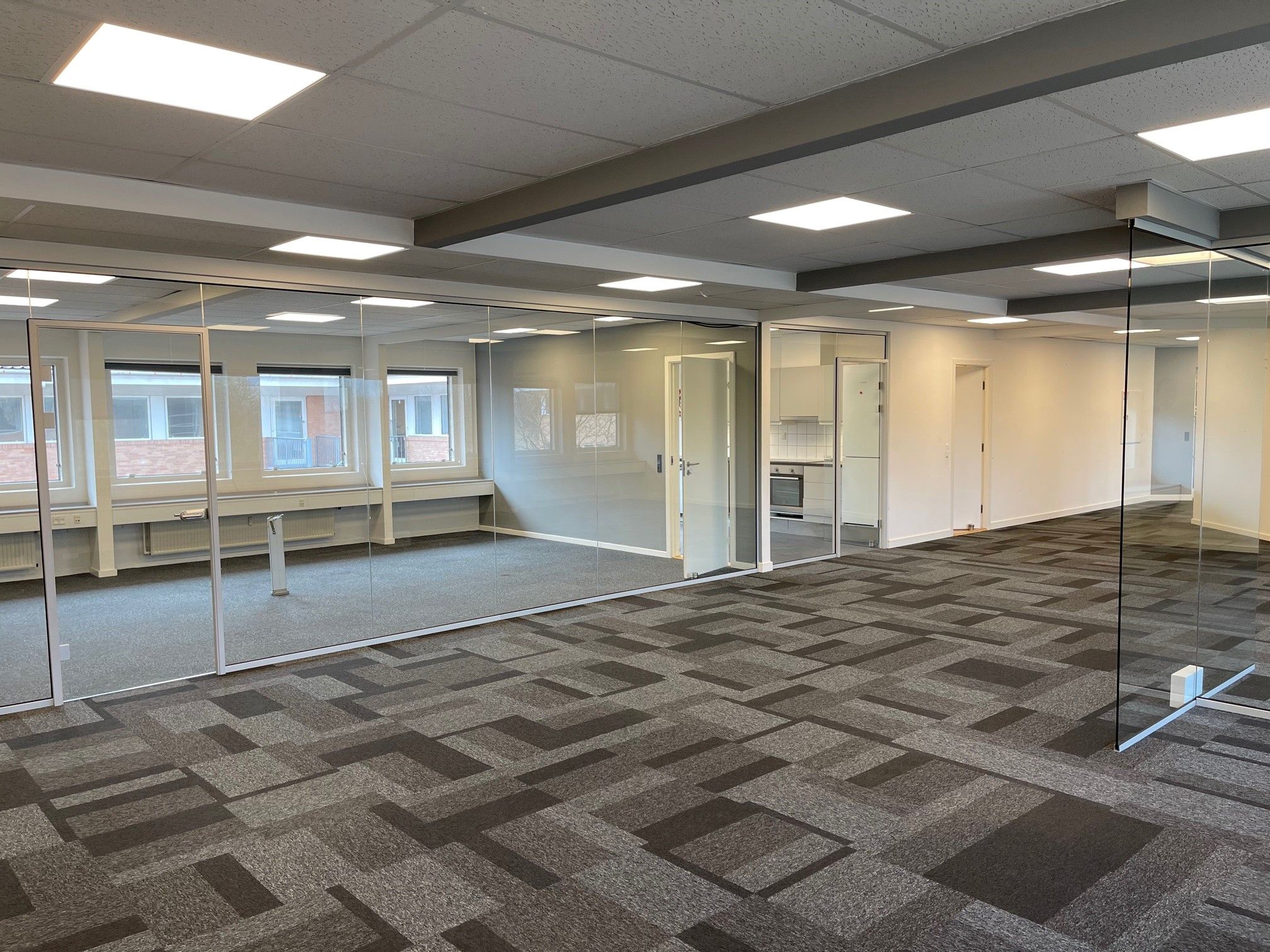 Et moderne kontor med glasvægge og lysegulv samt hvide vægge og lyse loftsbelysninger. Et kabinet med hvide skabe og en hvid