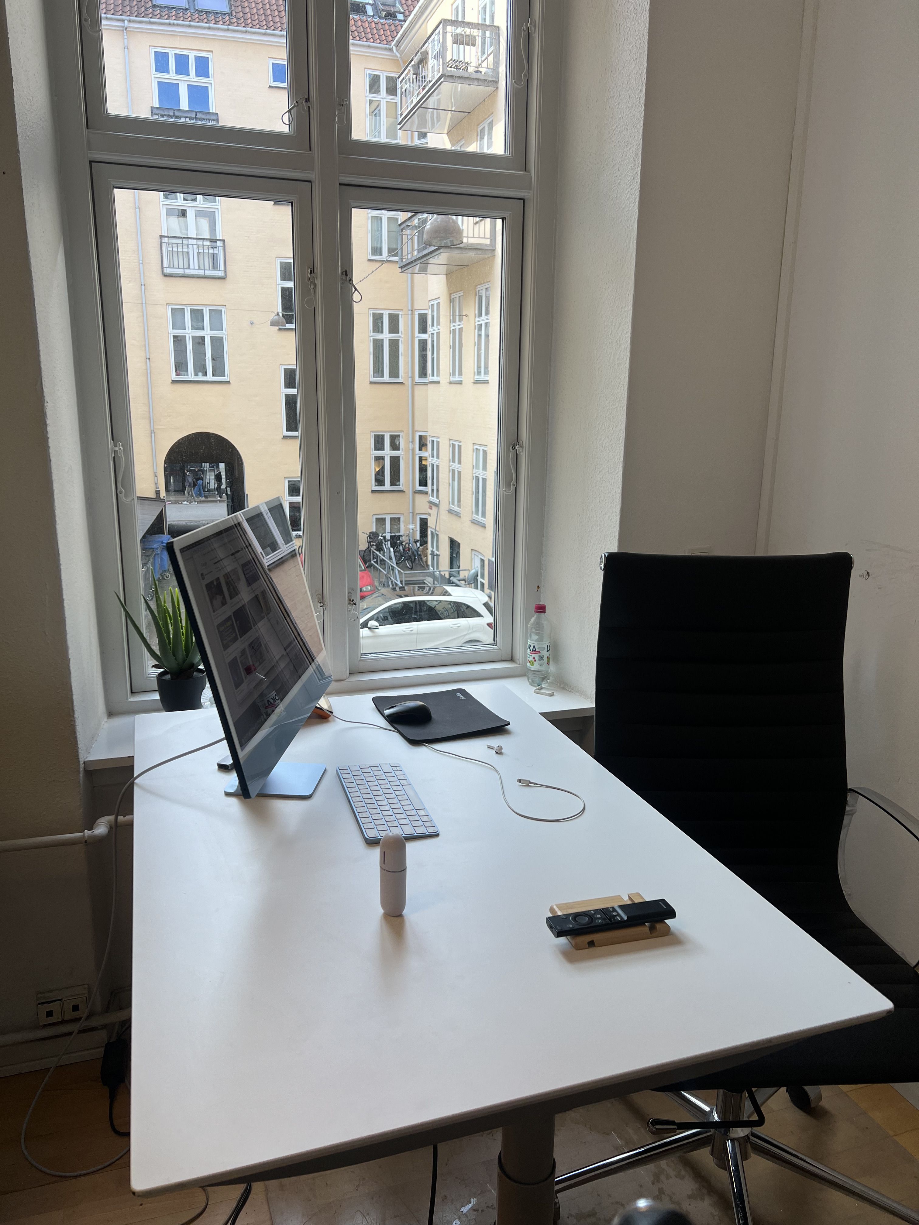 Rundt mødebord med computer og tastatur med københavn bagved. Også en plante og en fjernbetjening er placeret på bordet