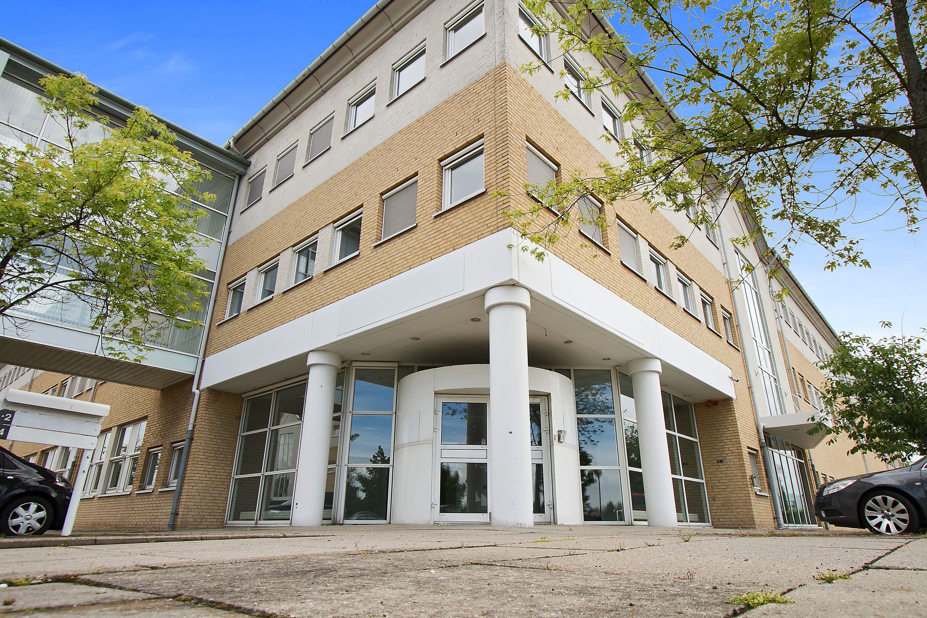 Et stort hvidt og gult bygning med mange vinduer og døre samt en indgangsparti med to store glasdøre og to hvide søjler