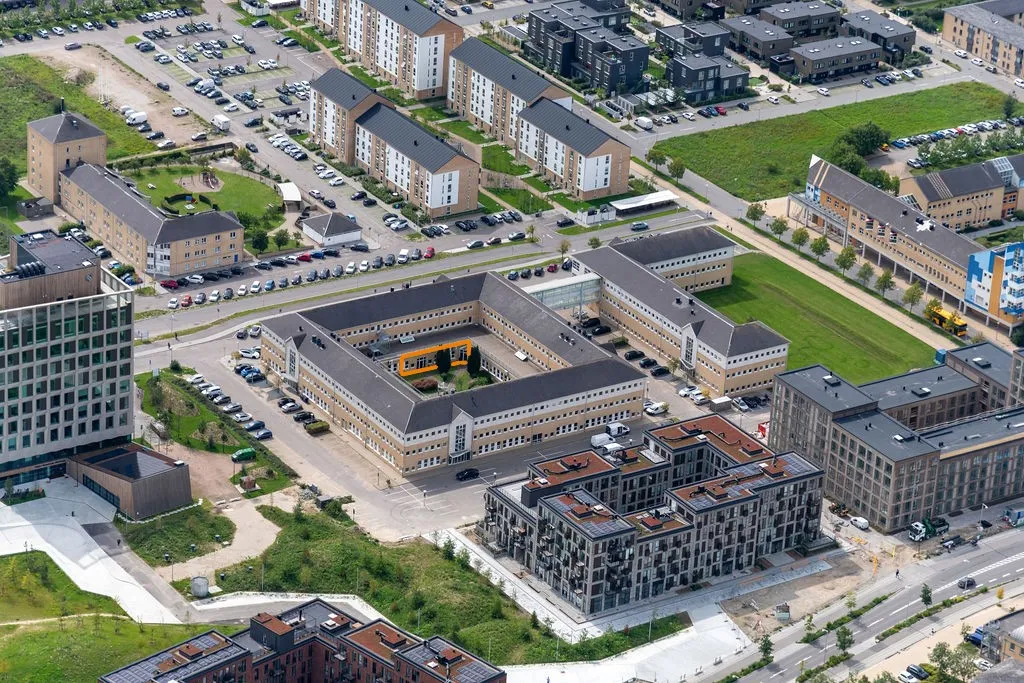 Moderne bygninger med parkeringspladser og grønne områder ligger på Spotorno Alle 2-10. En byggemaskine og en bus er også