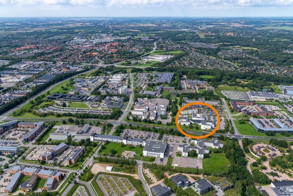 Byens forretningsdistrikt med mange bygninger, parkeringspladser og grønne områder, hvor en stor bygning er omkranset af en