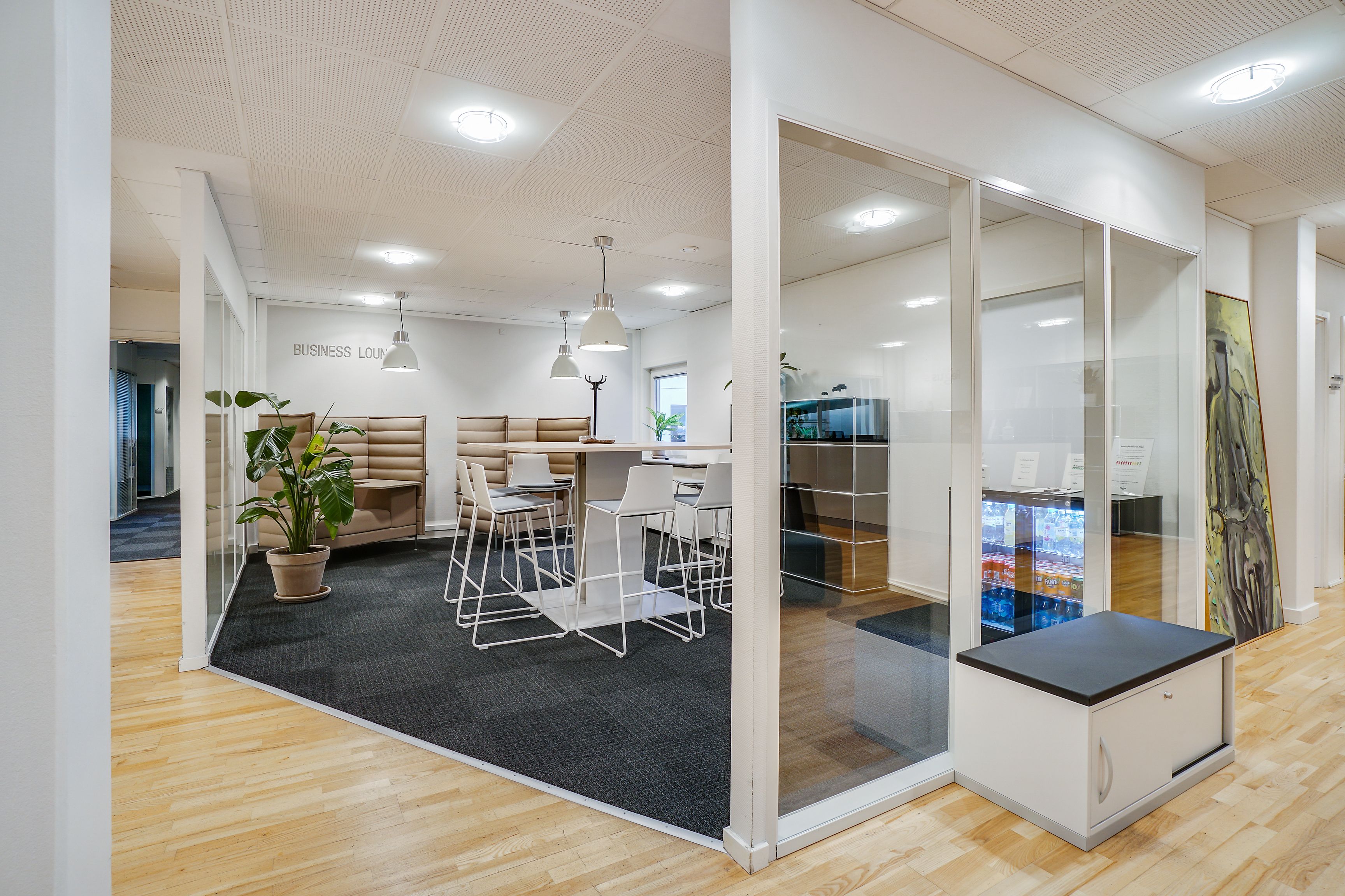 Kontorlokaler med højt loft og moderne interiør, hvid gulv, sofaer, borde og stole samt glasvægge