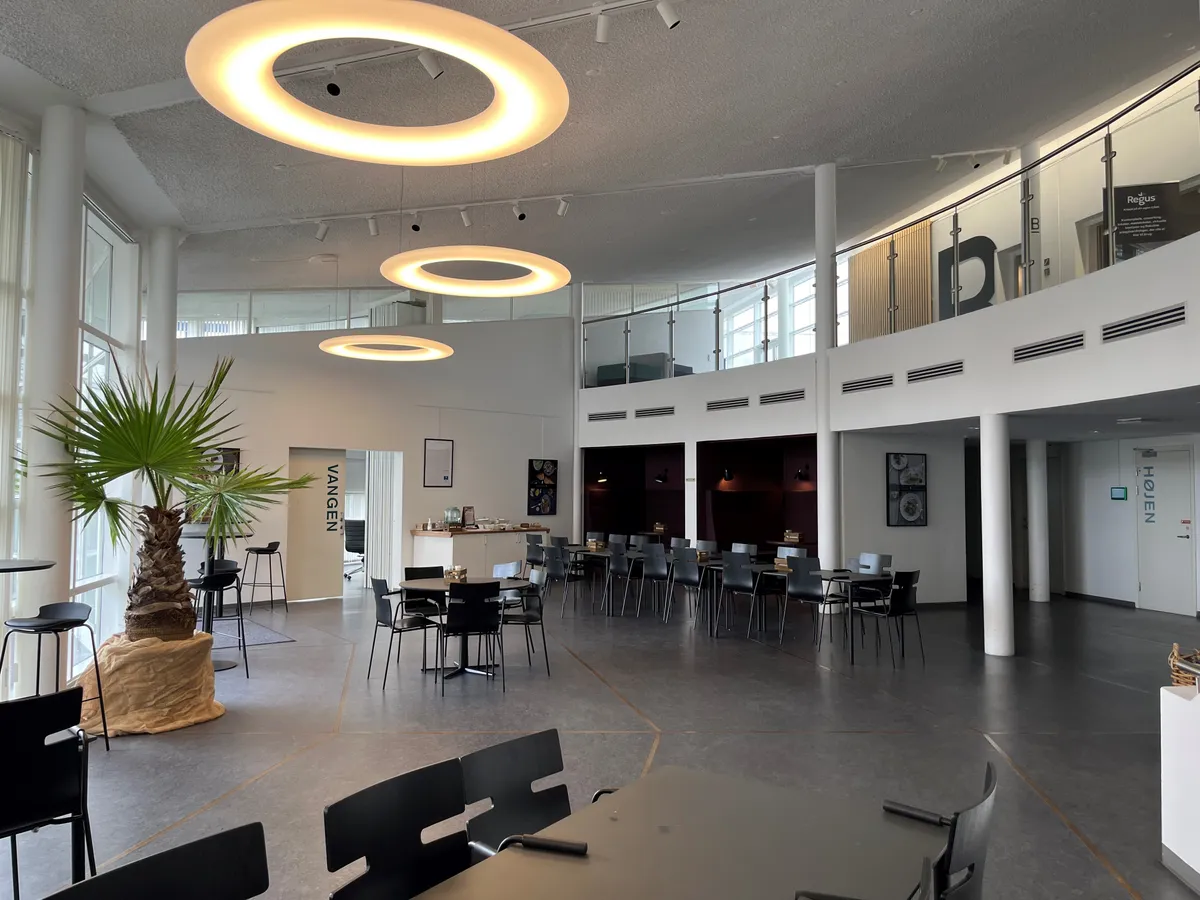 Moderne mødelokale med to runde hængelampe og stolpe af hvid glas. Her er et område med spisestue, der er delvist dækket af