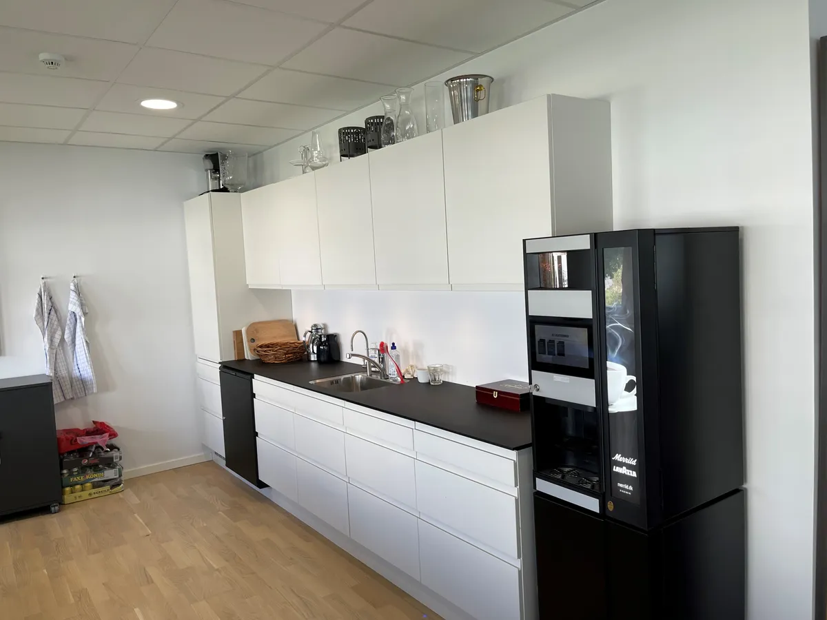 Hvidt køkken med højloft og lysekroner, køkken med hvide vægge og sort bordplade, og en moderne sort kaffemaskine placeret