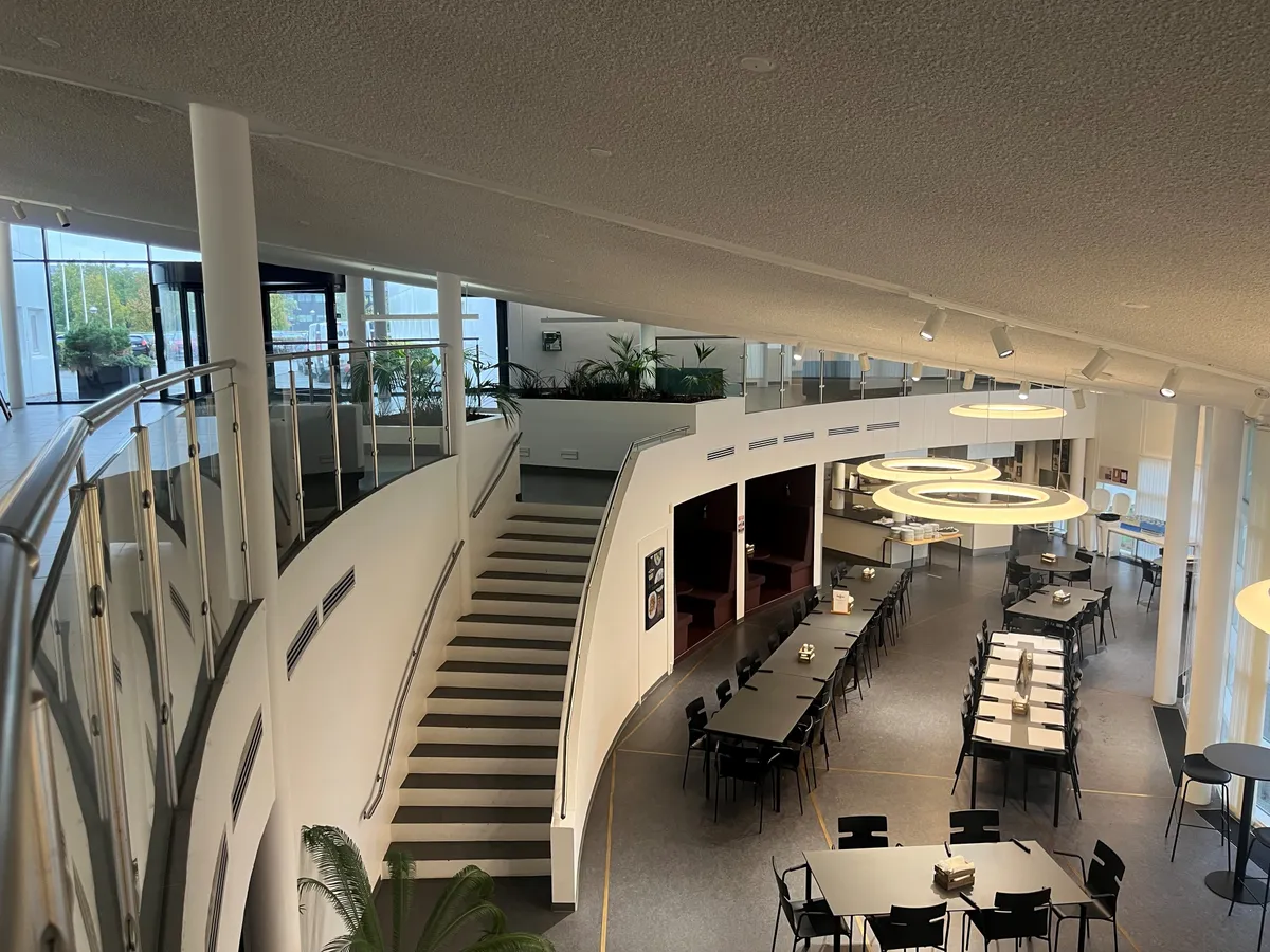 Inde i restauranten med runde loftslys og gulv. En lang bordrække med bord og stole. En lang stige med håndtag. Foran