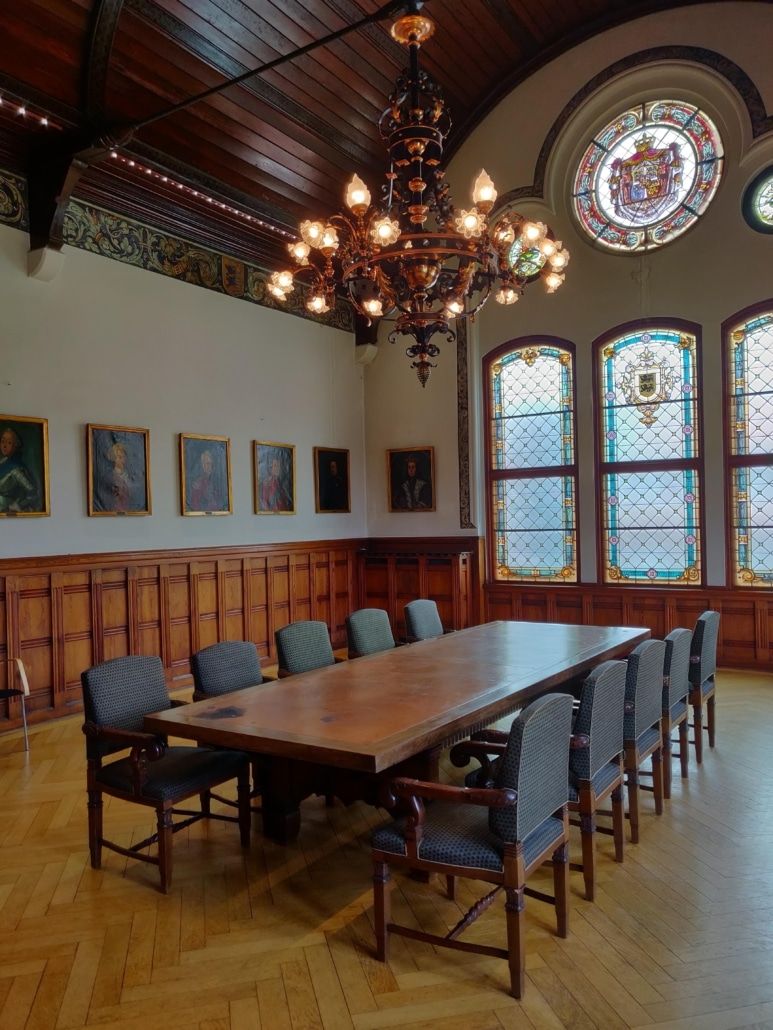 En konferencesal med lyse farver, krydsfinerbelagte gulve, møbler og store vinduer med våbenskjoldglas