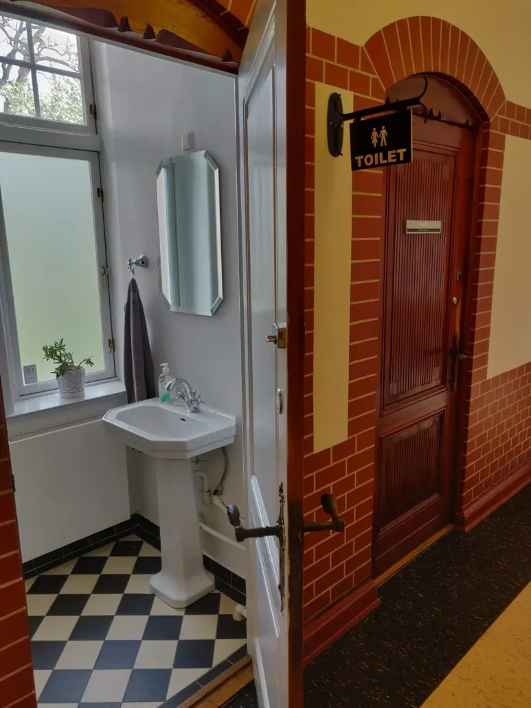 Toilet med sort og hvid gulvfliser og en spejl over et vask. Toiletdøren er brun og står åben