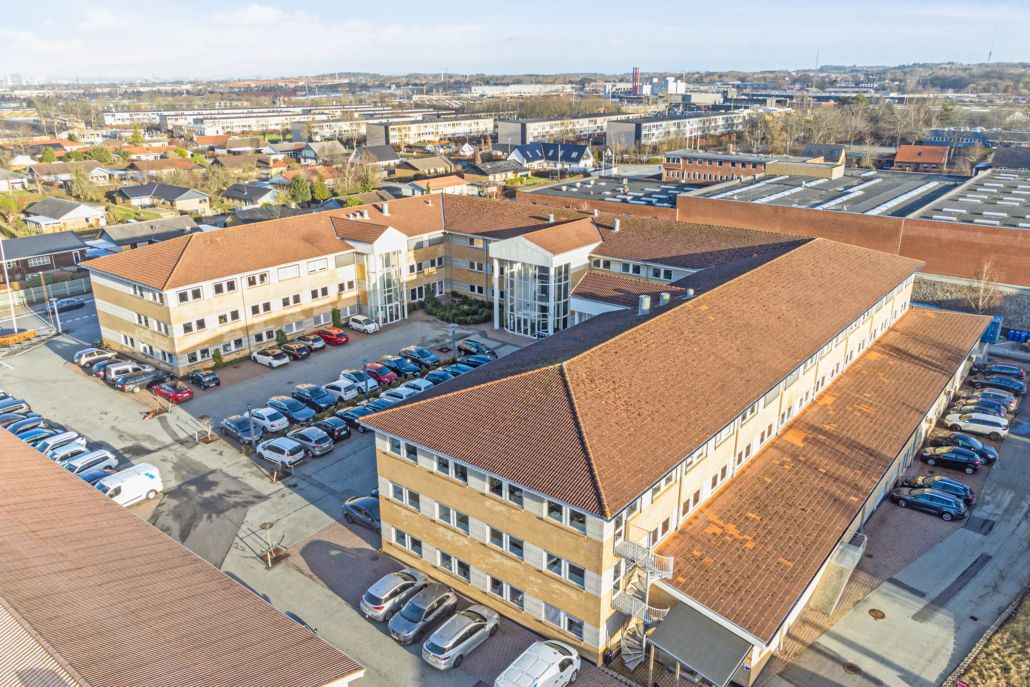 En masse biler parkeret foran Voxeværket i Aarhus, der er bygget af lysebrune mursten og har røde tagdækninger