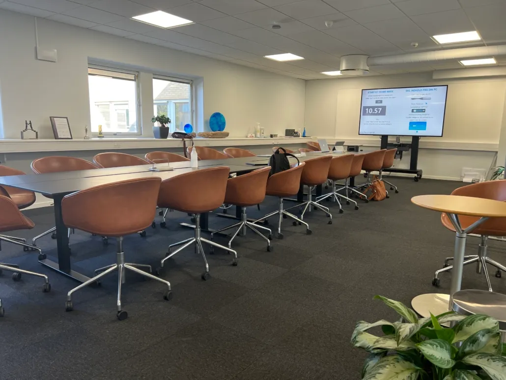 Et stort mødelokale med en stor tv-skærm og flere borde og stole