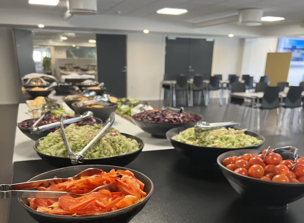 Buffet med salat, tomater, gulerødder og serveringsredskaber på en serveringsbord i et lokale