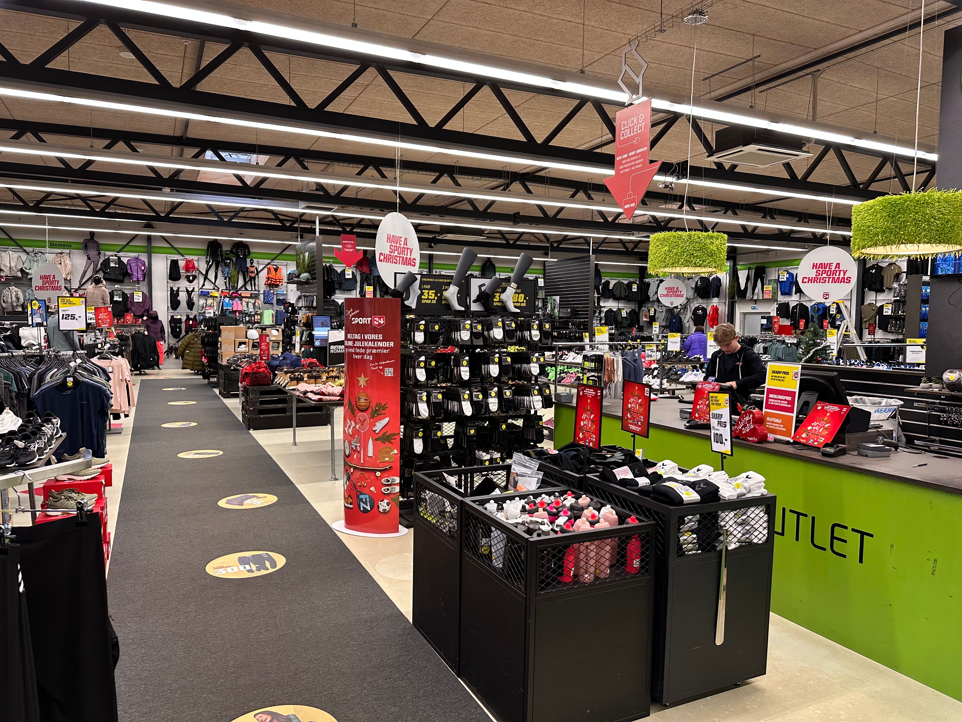 Sportbutik med udvalg af tøj, fodtøj og sportsudstyr, opdelt i afsnit med salgsskilte og rabatter, samt et kastebord med