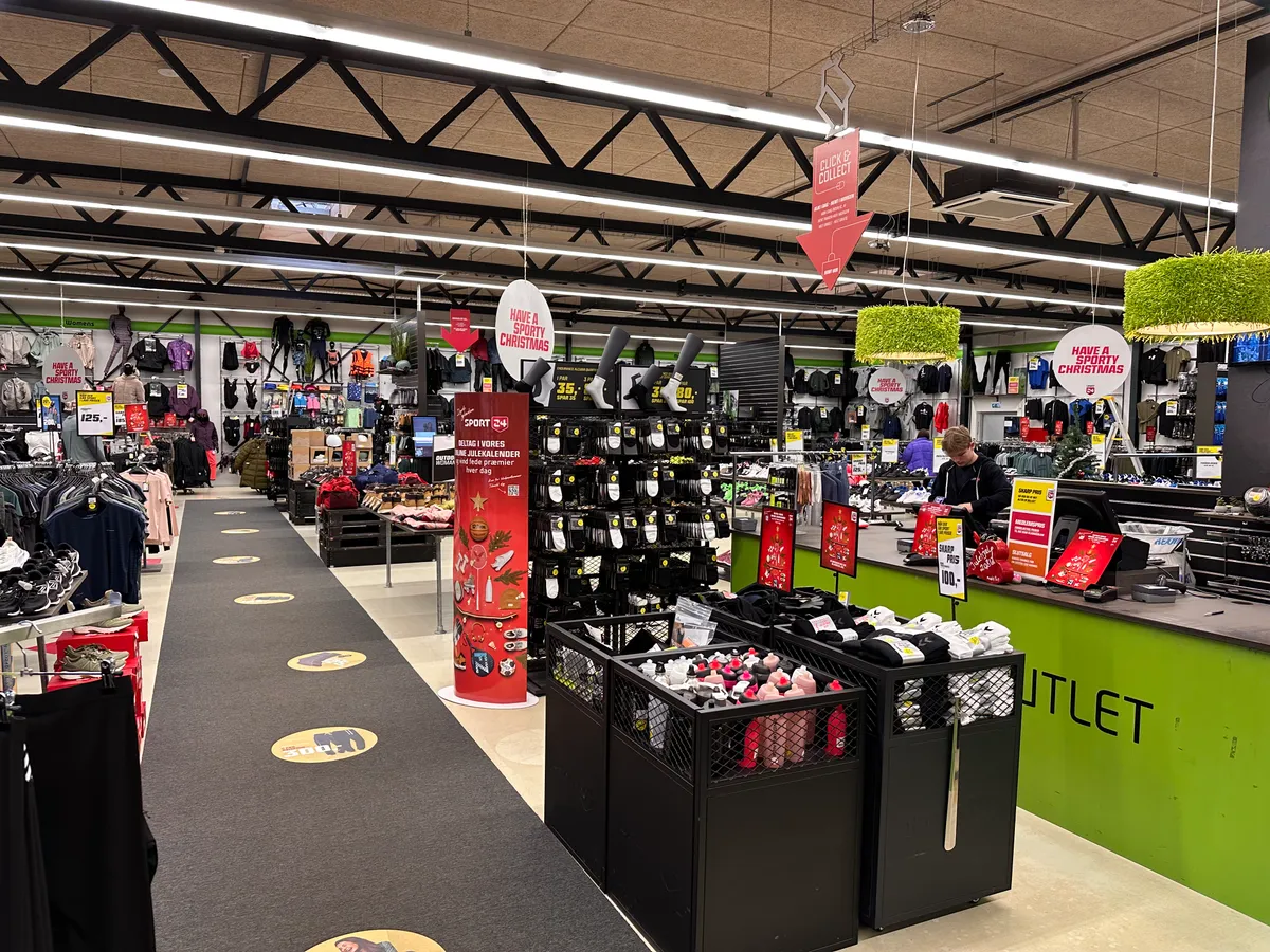 Sportbutik med udvalg af tøj, fodtøj og sportsudstyr, opdelt i afsnit med salgsskilte og rabatter, samt et kastebord med