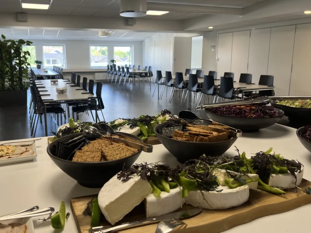 Buffet med krydderurter, salat og smøreost på træskærmet tallerken i Voxeværkets mødelokale med vinduer og stole