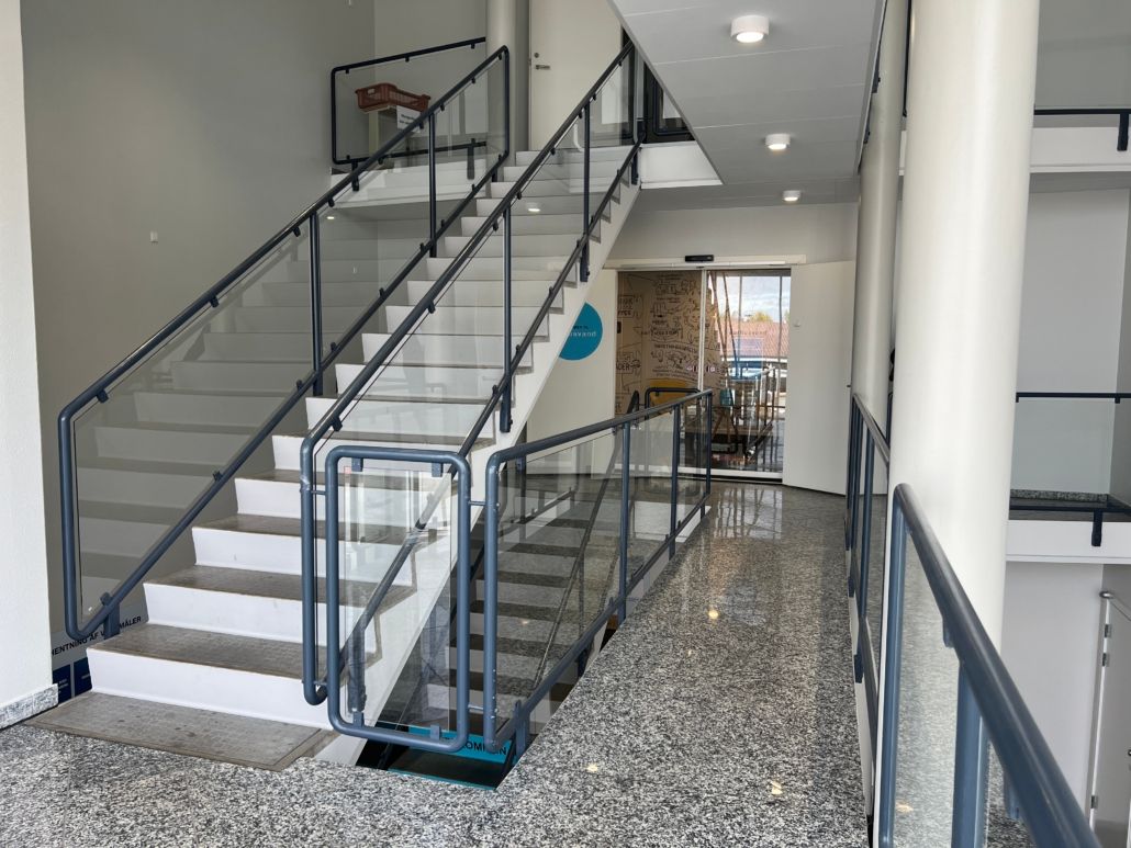 Moderne lobby med trappe og glasrækværk, gulvet er lavet af granit, og der er åbninger med trapper og et skriftligt design