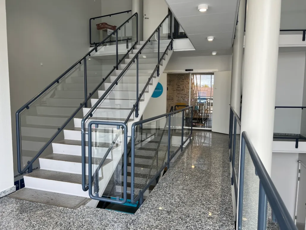 Moderne lobby med trappe og glasrækværk, gulvet er lavet af granit, og der er åbninger med trapper og et skriftligt design