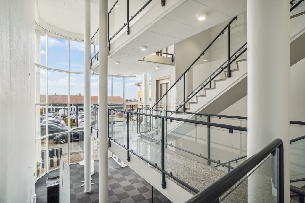 En stor atrium med glas, metal og marmor. Tre gange med høje stiger og slanke søjler. Parkeringsplads med biler og bygninger.