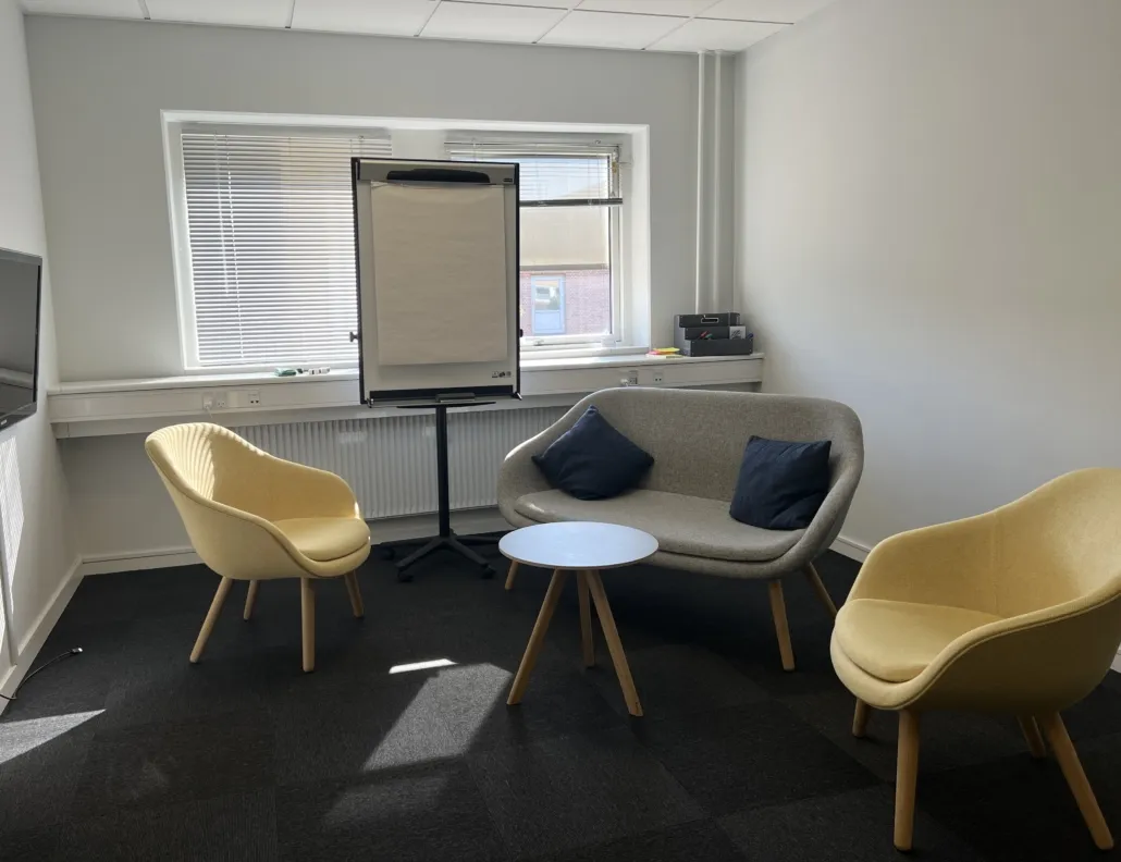 En lydstyrkeforstærker står ved vinduet med et whiteboard, og der er en tv-skærm og et bord med to høje stole