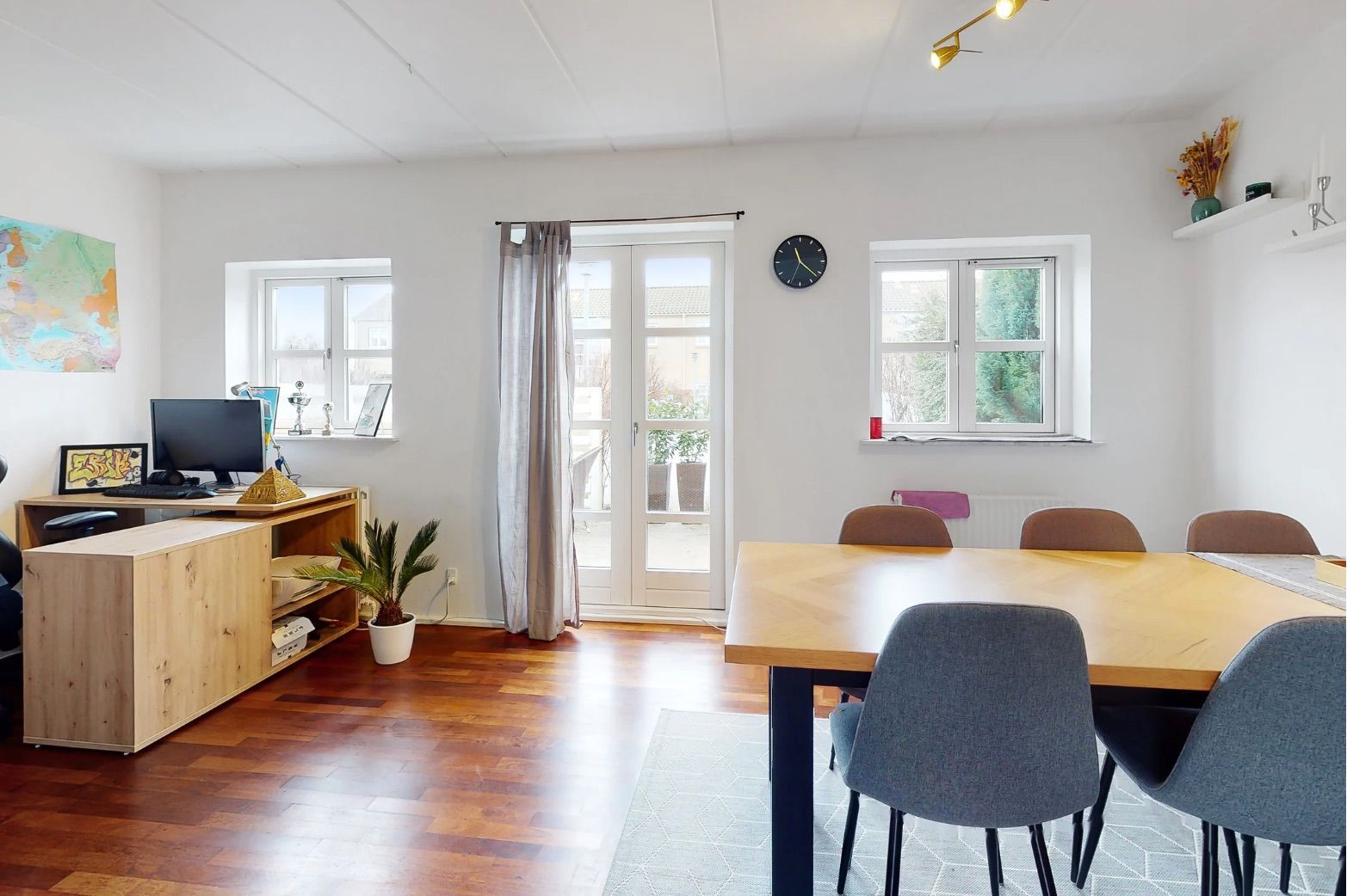 Et moderne hus med lyse møbler og trægulve, en stue med bord, stole og plante og et arbejdsområde med computer og skrivebord