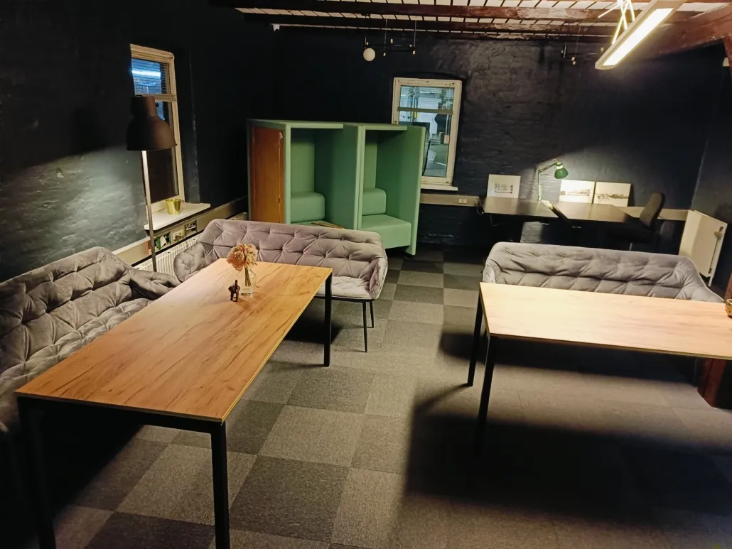 Indvendigt i en kontorlokaler er der møbler og skriveborde, der er placeret i en stor stue med lysegulv og grønne møbler