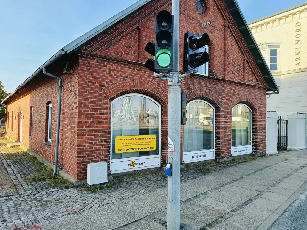 Tegn på skilt for kørebaneforlængelse i Frederikshavn. Vindue med udsigt over havnen og vejside med røde pletter.