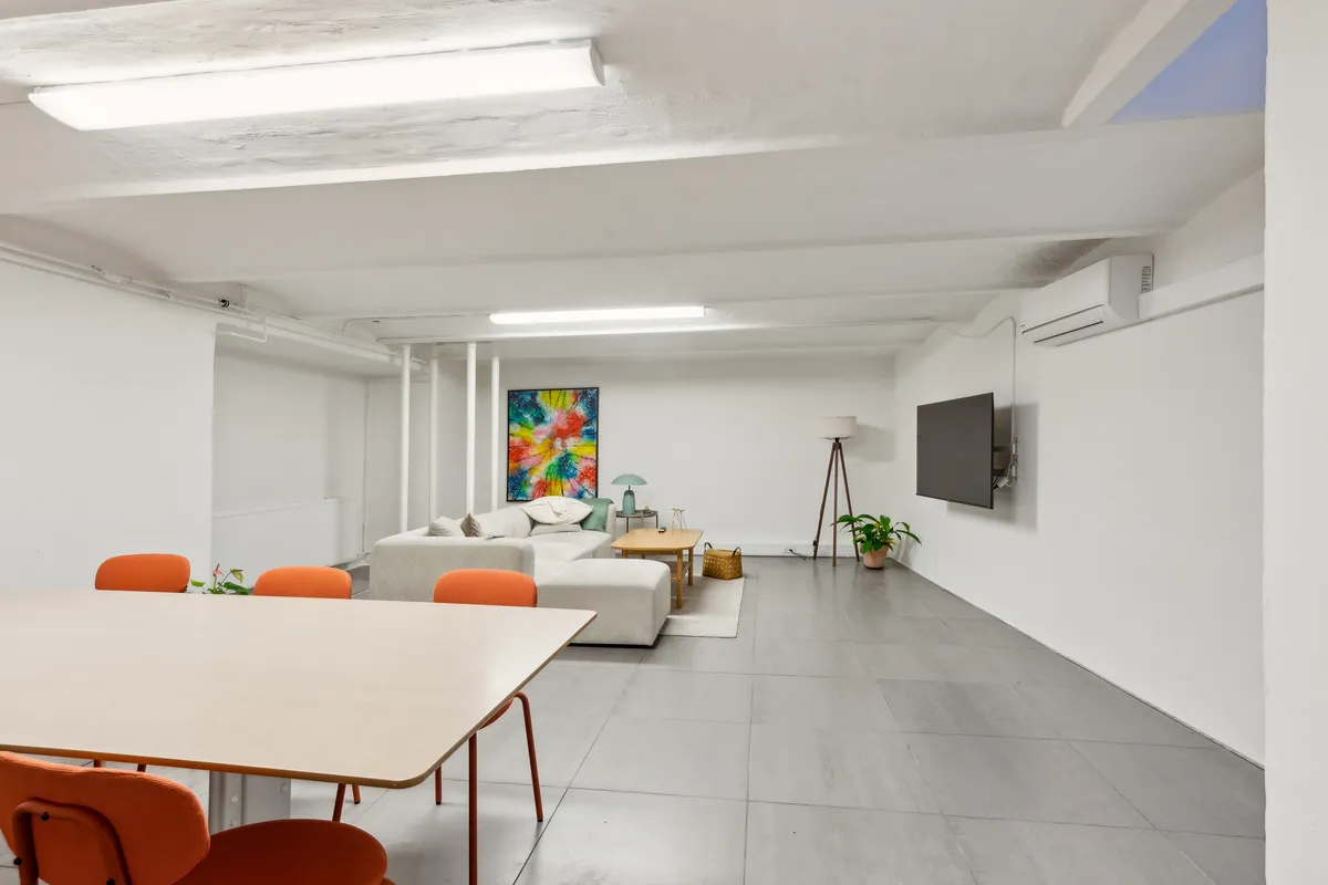 Moderne og pænt indrettet lejlighed med hvidt og gråt design, runde orange stole, tv og kunstværk på væggen