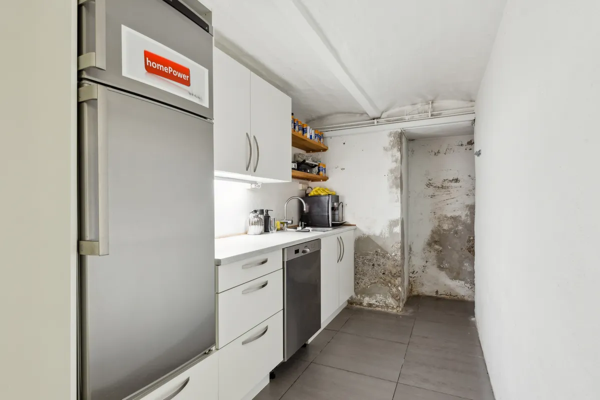 En lukket køleskab med HomePower-logoet og en rusten væg i et renoveringsbedyrvet køkken med et vaskemaskine, ovn og håndvask